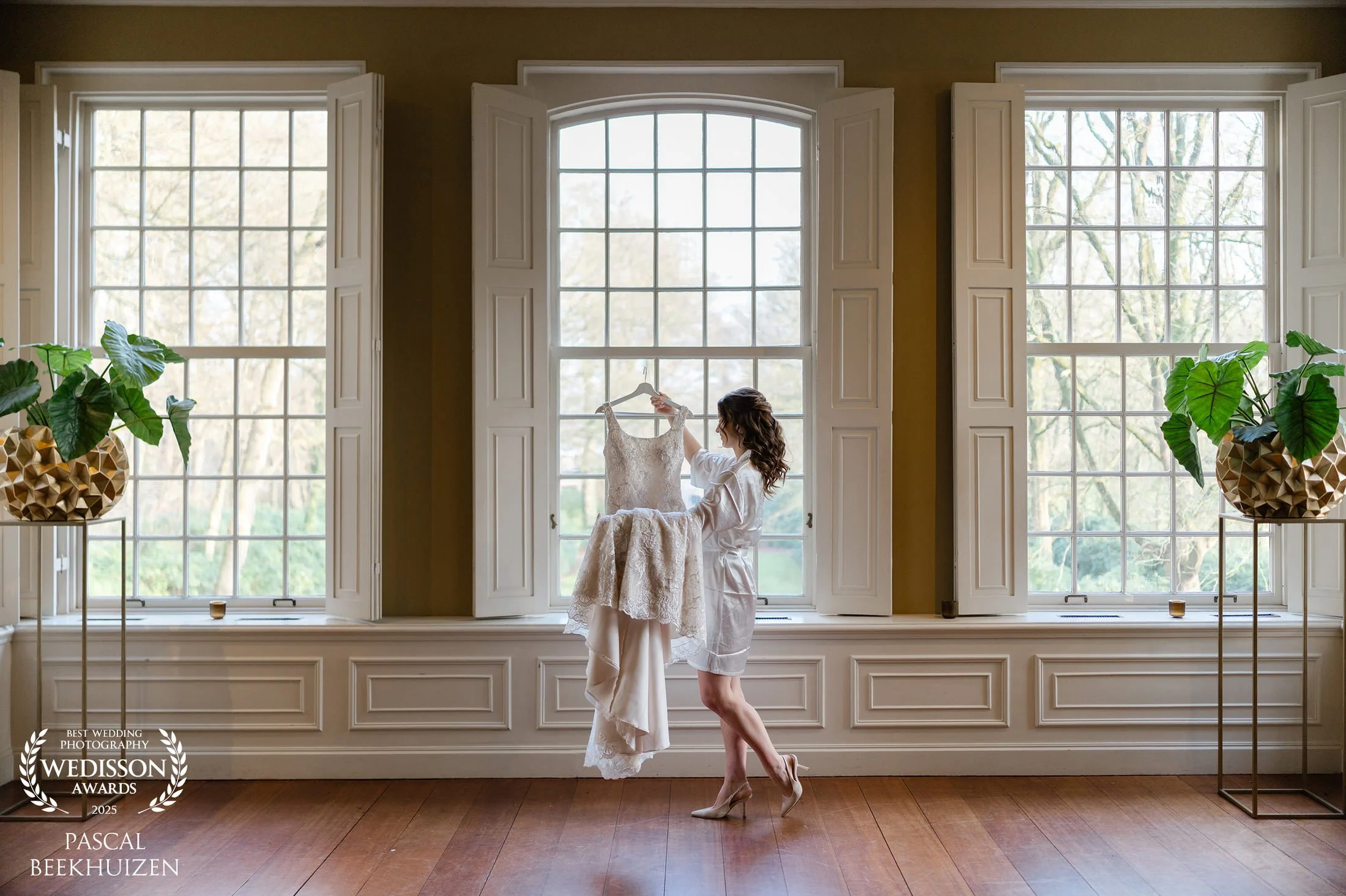 Get ready moment tijdens een winterbruiloft bij Buitenplaats Sparrendaal, bruid pakt haar jurk bij het raam, trouwfotograaf Gelderland