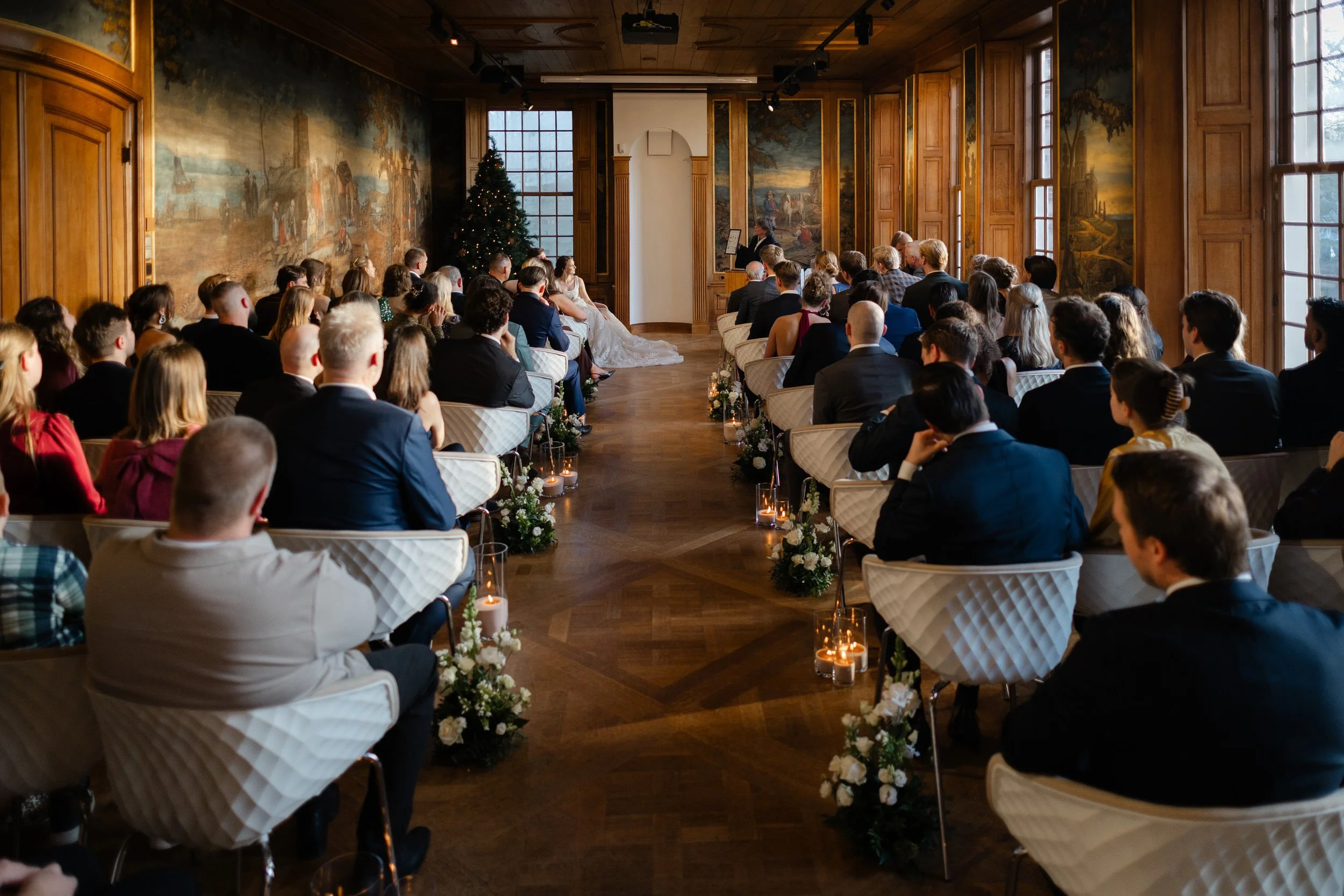 Gasten zitten klaar tijdens de ceremonie in een stijlvolle trouwzaal, breed reportagebeeld van de bruiloft bij Buitenplaats Sparrendaal.