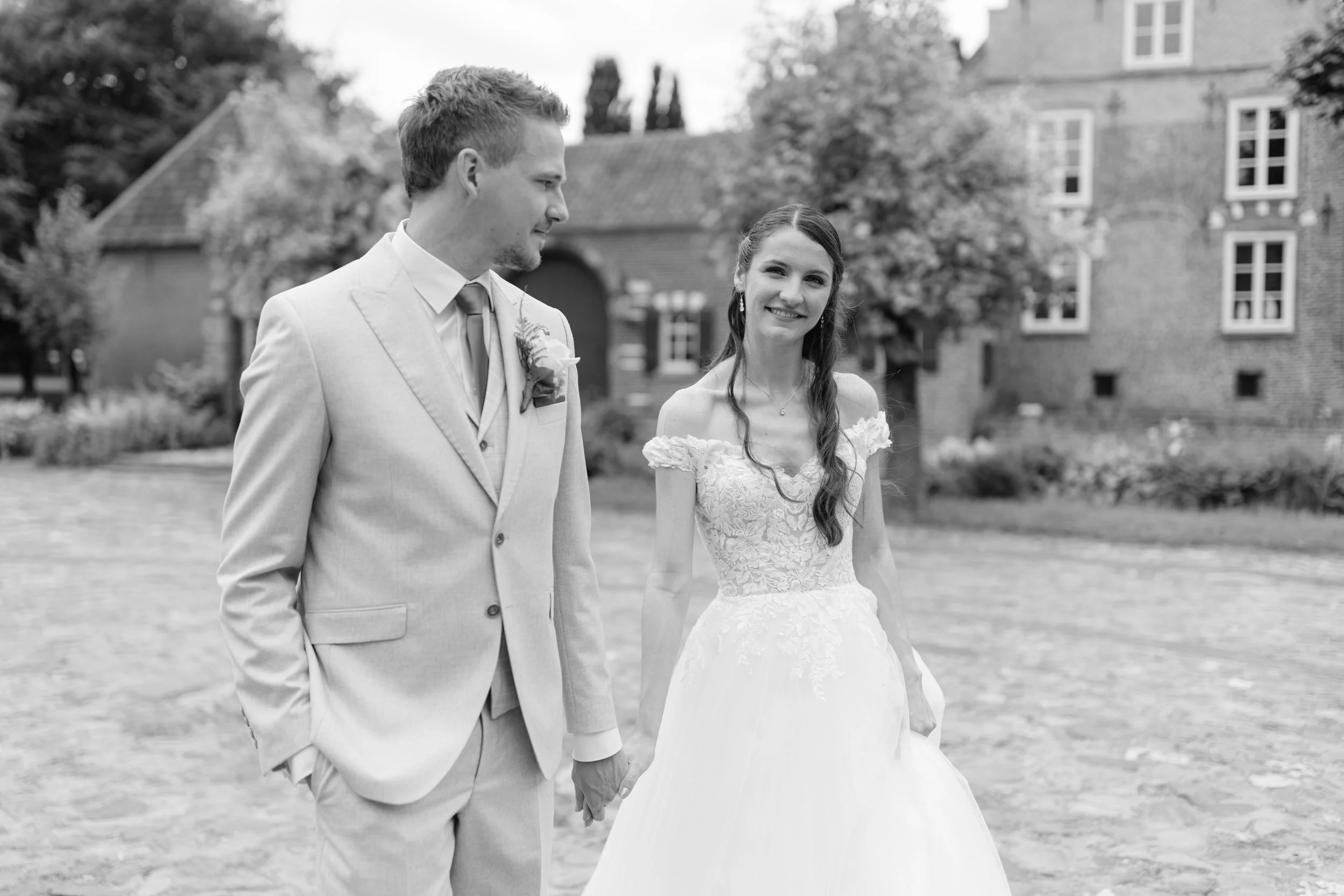 Bruidspaar loopt hand in hand over de binnenplaats, zwart wit trouwfoto met een rustig en stijlvol moment