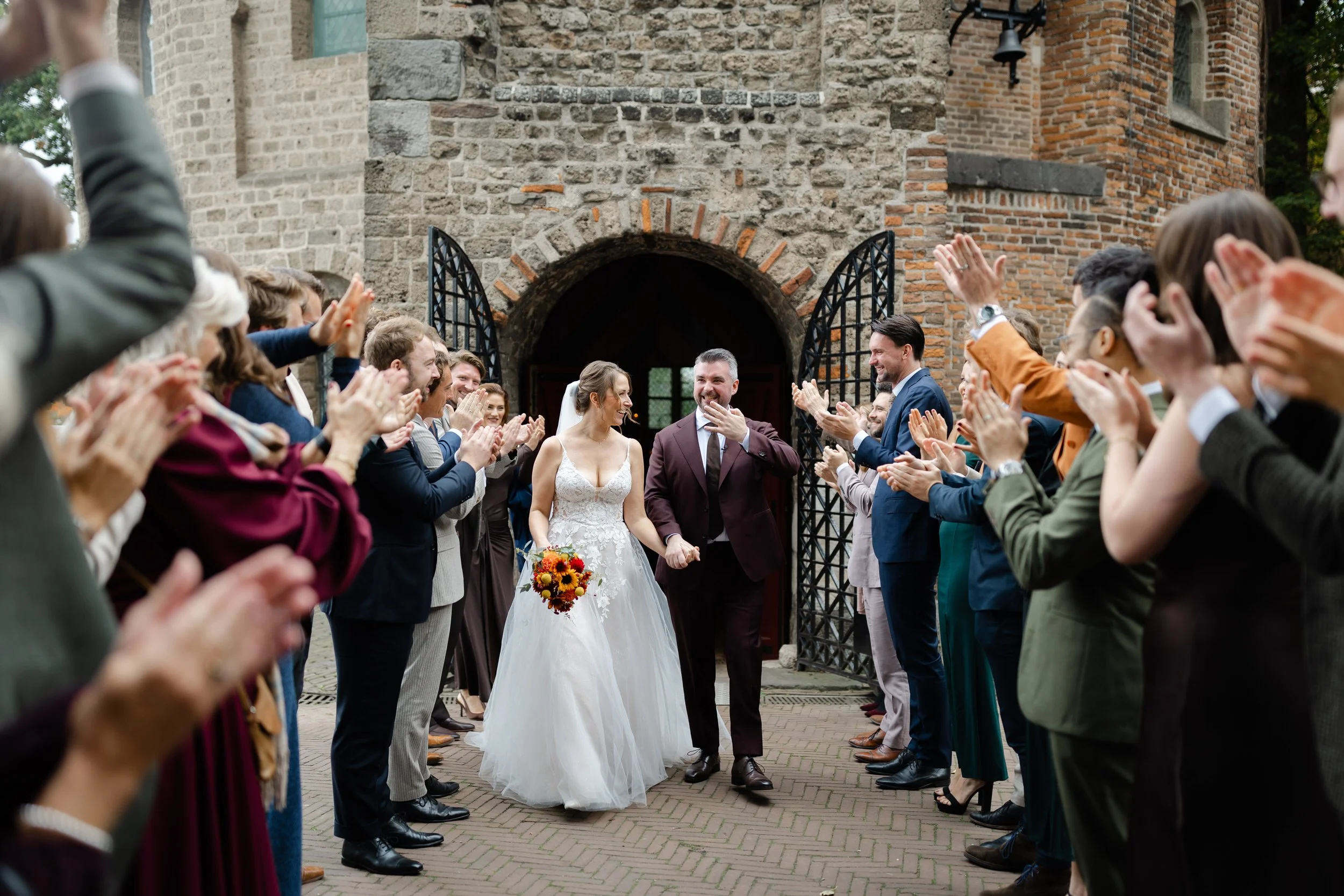 Bruidspaar loopt door een erehaag van applauderende gasten na de ceremonie, spontaan moment op de trouwdag