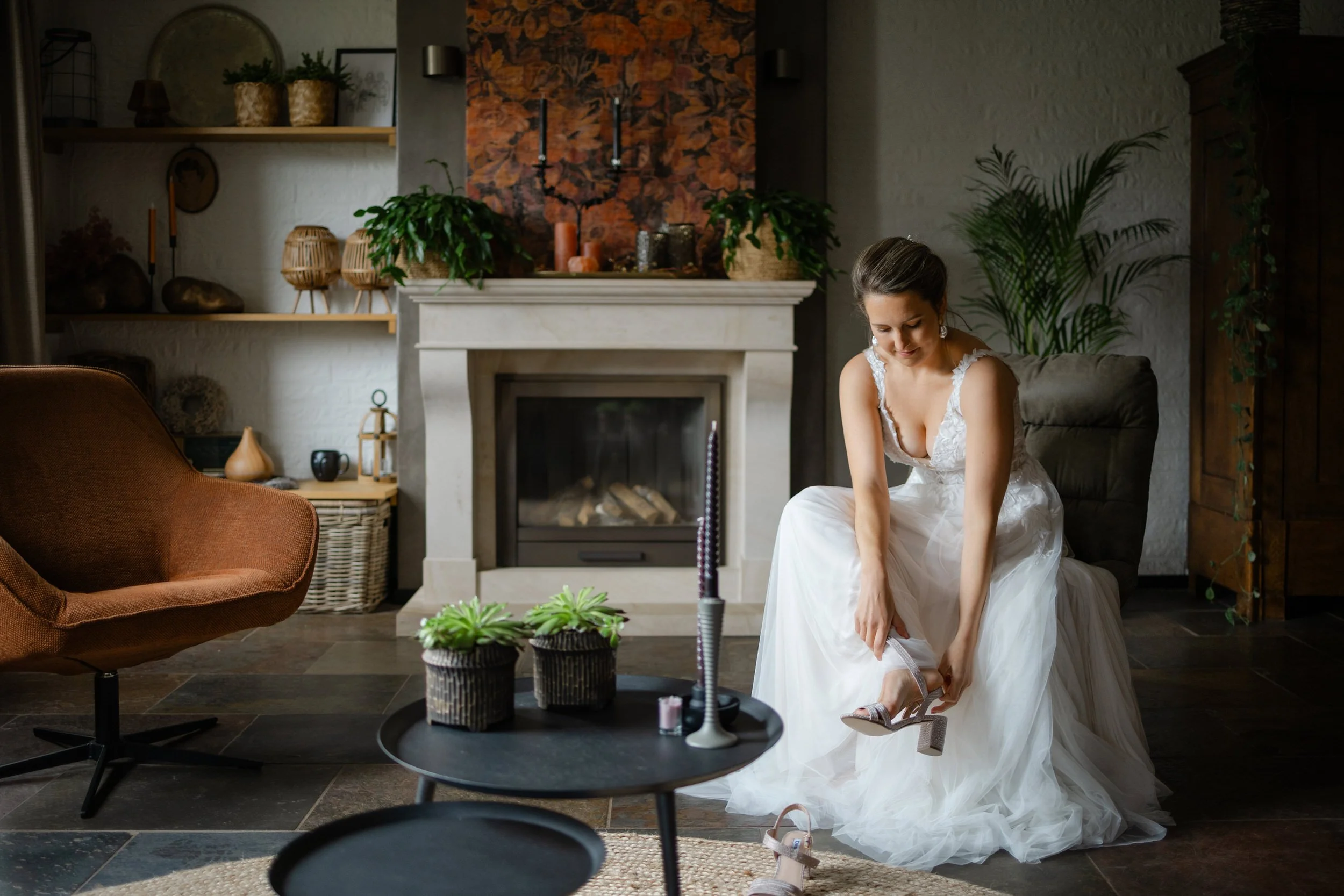 Bruid doet haar schoen aan bij de open haard tijdens de voorbereidingen van de trouwdag, intiem moment in een warme setting