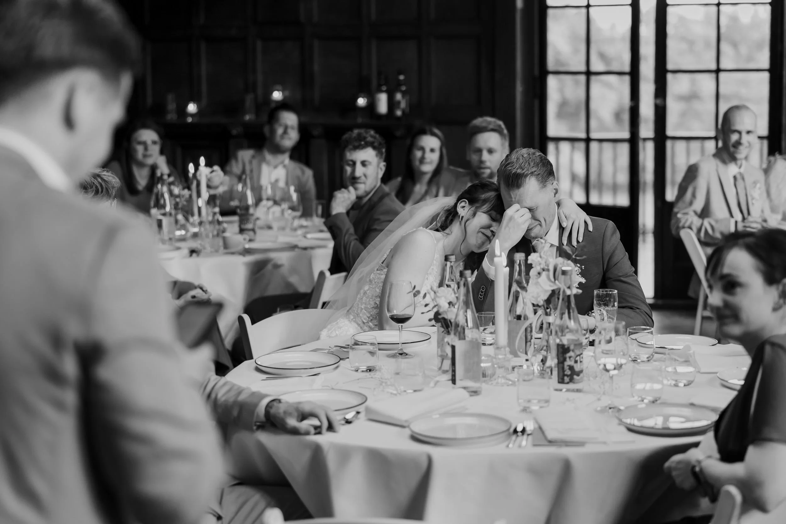 Bruid leunt emotioneel op de schouder van de bruidegom tijdens het diner, zwart wit foto vol gevoel en echte momenten