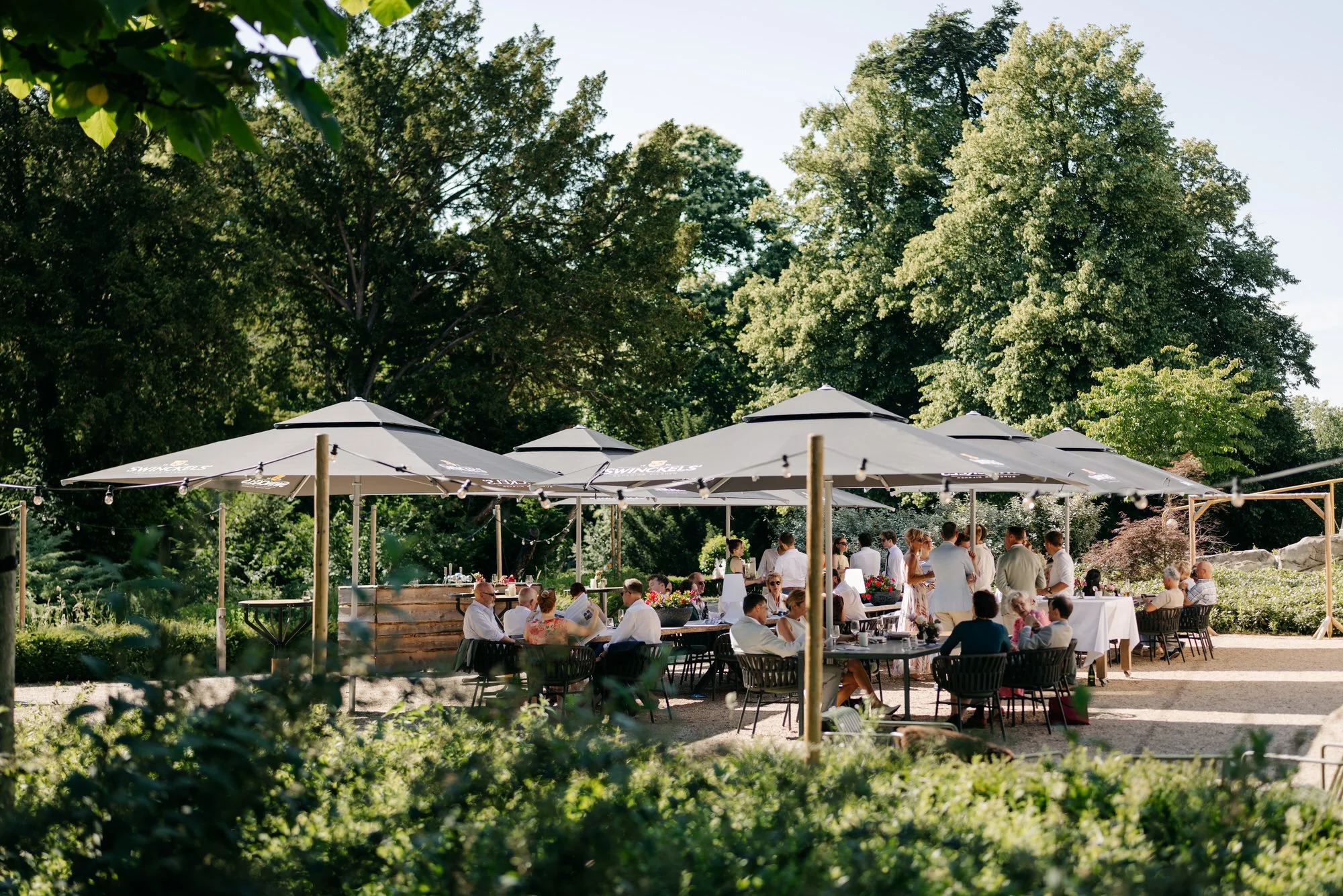 gasten genieten van de borrel onder parasols in de schaduw tijdens warme bruilof