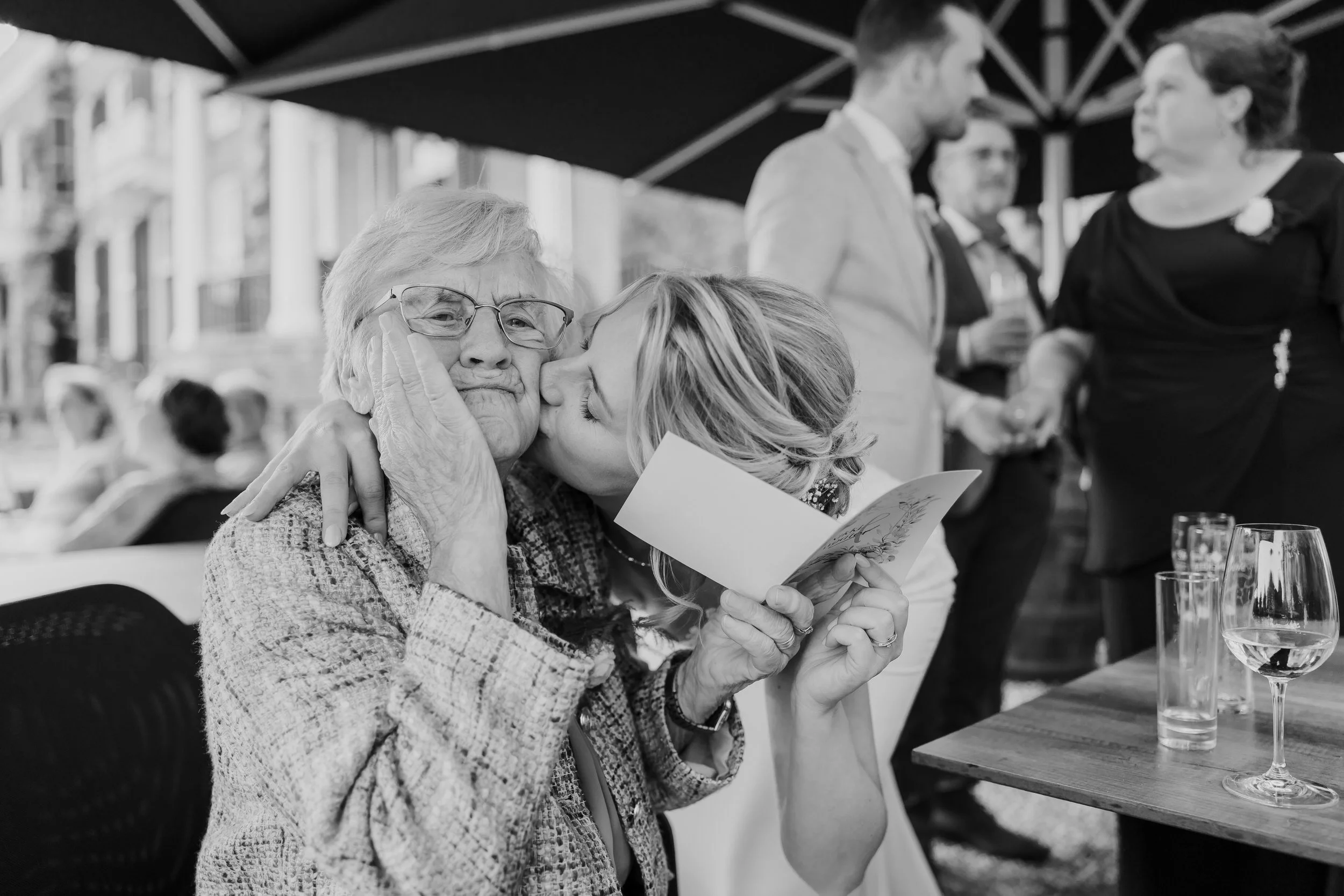 Bruid geeft haar oma een kus op de wang, zwart wit trouwfoto vol warmte en emotie