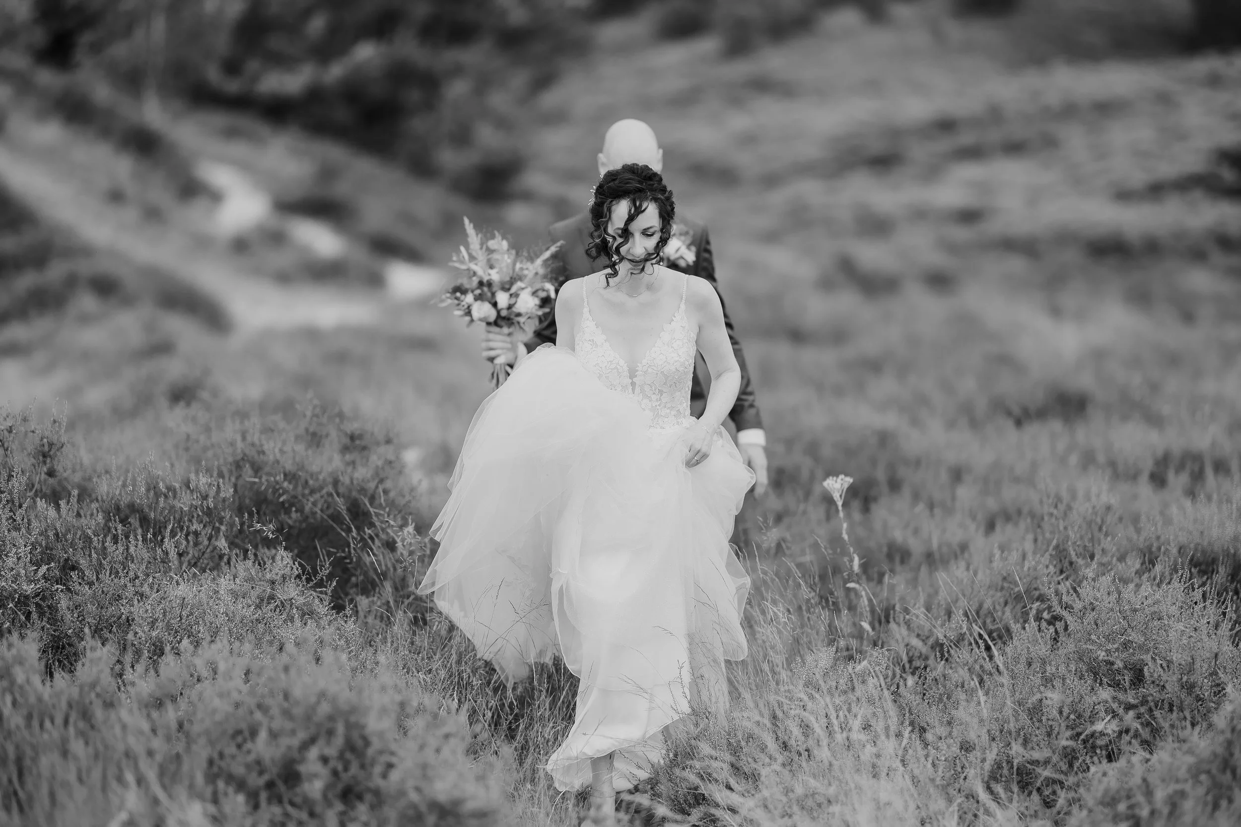 Bruid en bruidegom lopen samen door een heideveld, zwart wit trouwfoto met zachte beweging en natuurlijke uitstraling