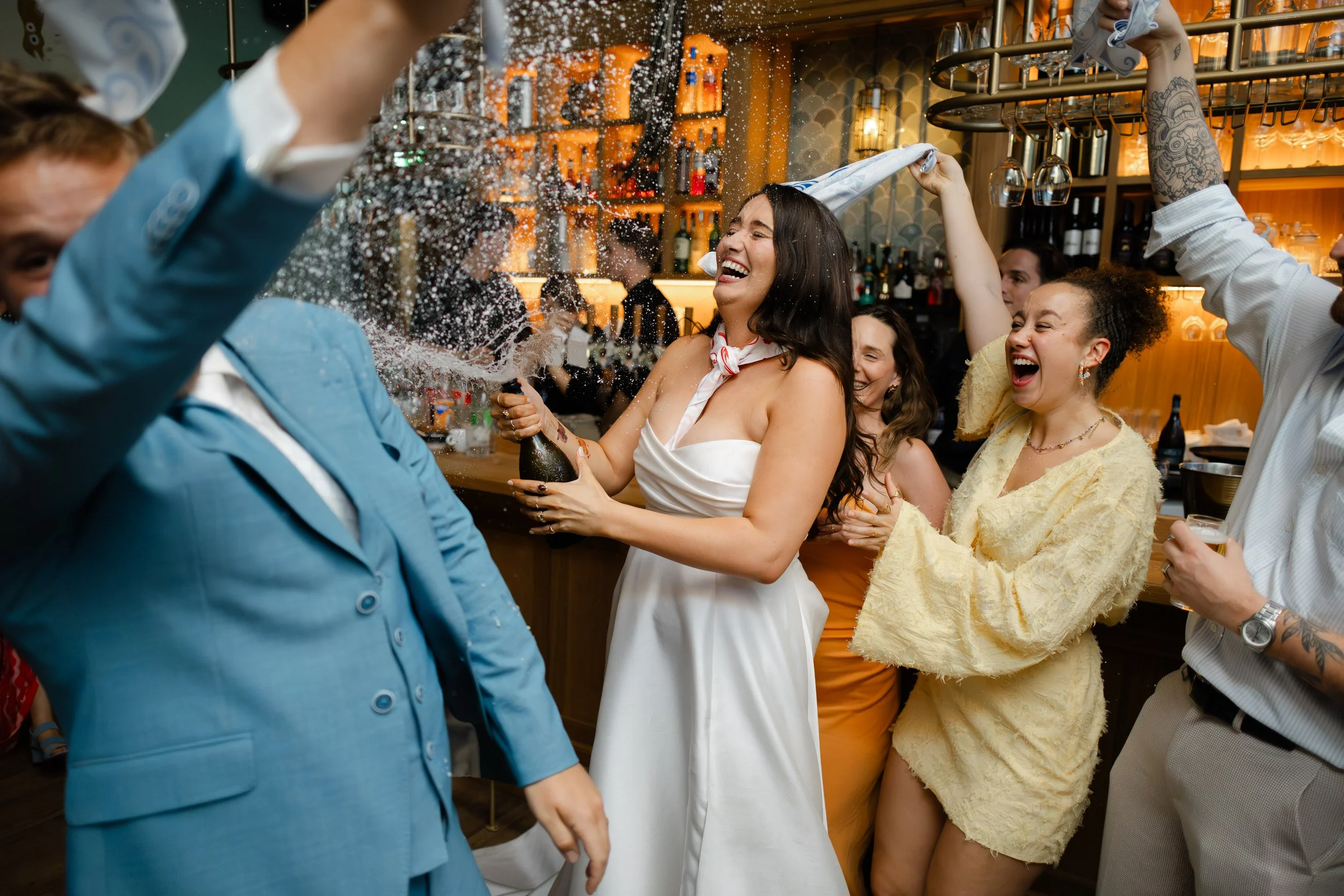 Bruid viert feest met vrienden terwijl champagne wordt gespoten, spontaan en energiek moment op de bruiloft