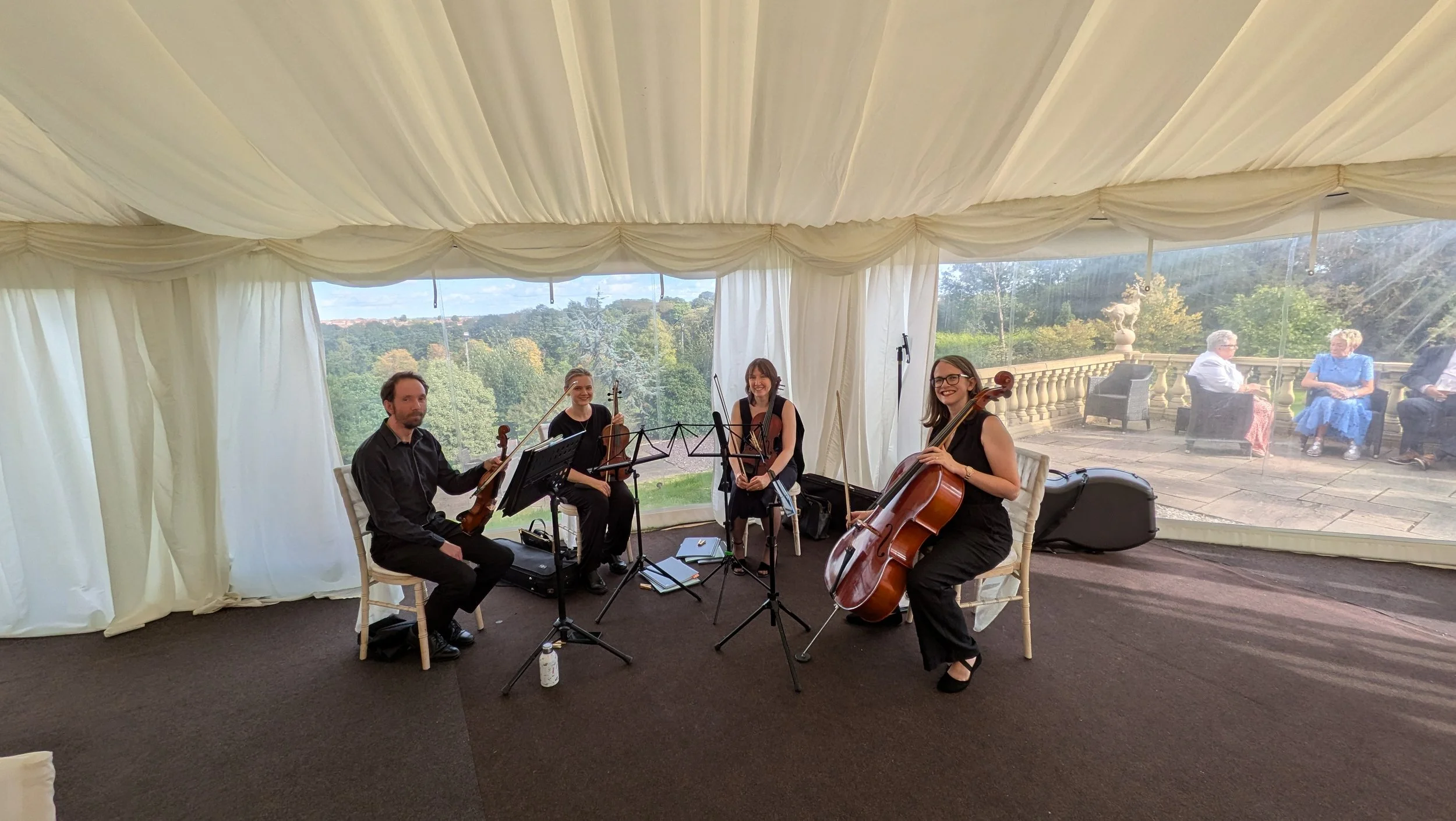 A string quartet pose, smiling to the camera, sat inside a marquee