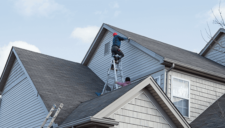 Workers on ladders installing siding on a residential home.