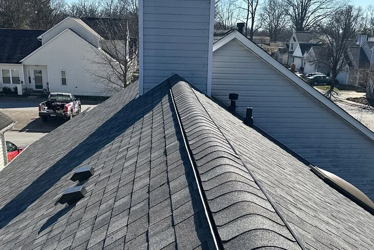 Completed dark gray architectural shingle roof viewed from the ridge line showing clean hip and valley lines in a suburban neighborhood