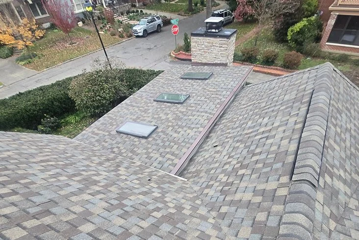 Newly installed gray blend architectural shingles on a residential roof with three skylights and a stone chimney viewed from above