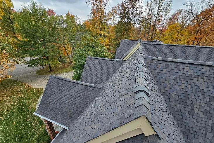 Completed dark gray architectural shingle roof with multiple peaks and valleys on a large home surrounded by fall foliage