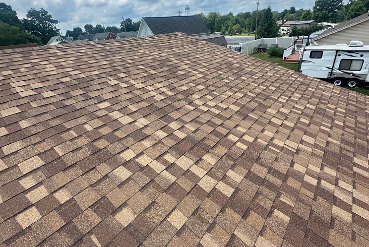 Close-up of a completed brown-tone architectural shingle roof on a residential home in a suburban neighborhood