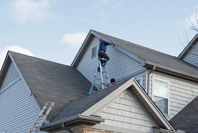 Contractors installing shingles on a high roof.