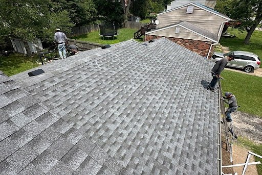 Roofing crew members finishing installation of gray architectural shingles on a residential roof viewed from above