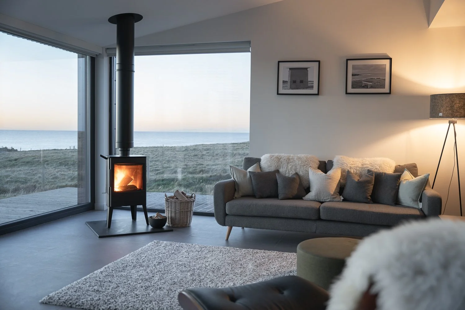 A beautifully designed living room featuring a comfortable sofa, a warm fireplace, and a stylish lamp. Floor-to-ceiling windows offer stunning ocean views, flooding the space with natural light and creating a serene atmosphere. 