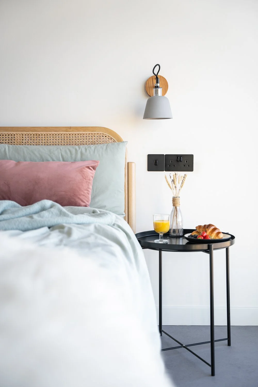 A cozy unmade bed with a bedside table showcasing a book, a glass of whiskey, and a small picture frame. This inviting scene emphasizes relaxation and comfort, perfect for those leisurely moments at home.