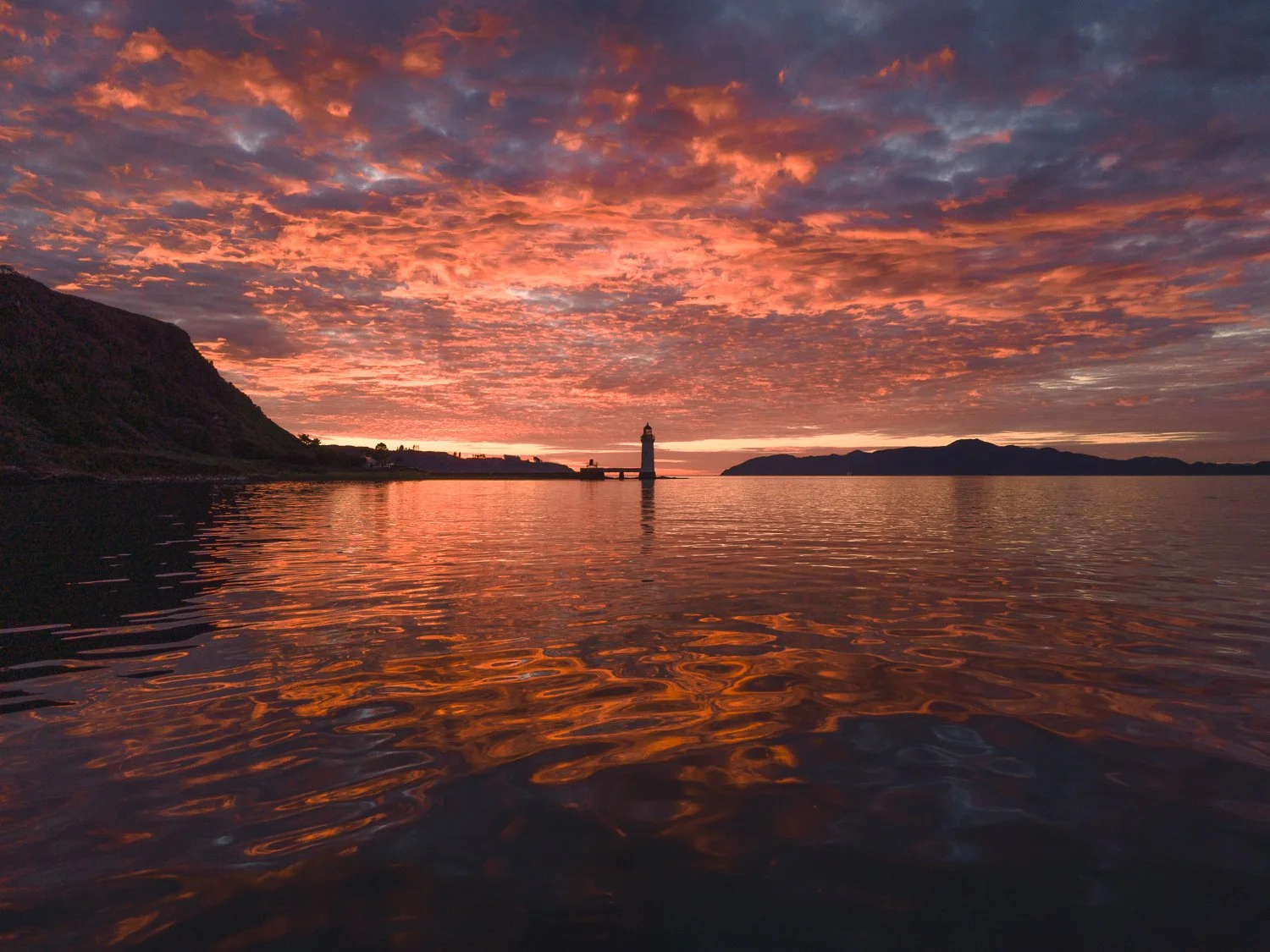 A breathtaking view of a Tobermory lighthouse with a stunning sunset reflected in the sea.