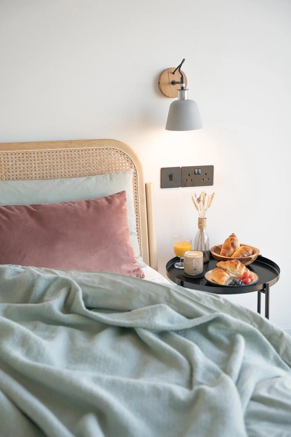 A cozy unmade bed with a bedside table set for breakfast, featuring fresh croissants, refreshing orange juice, tea, and vibrant fruit. This inviting scene captures the essence of leisurely mornings, perfect for promoting comfort and indulgence in hos