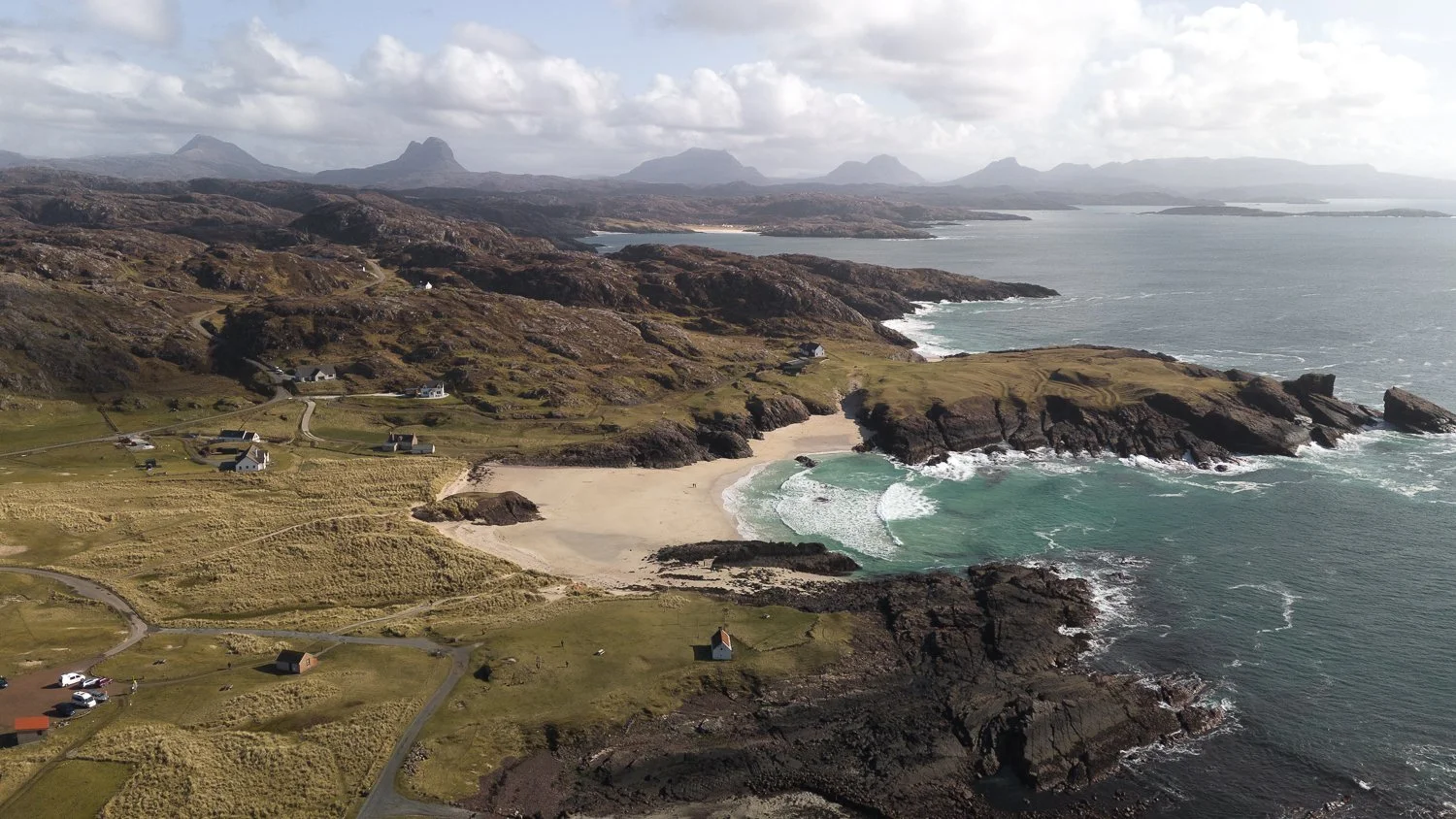 A panoramic aerial view of white sand beach with mountain peaks in the distance.