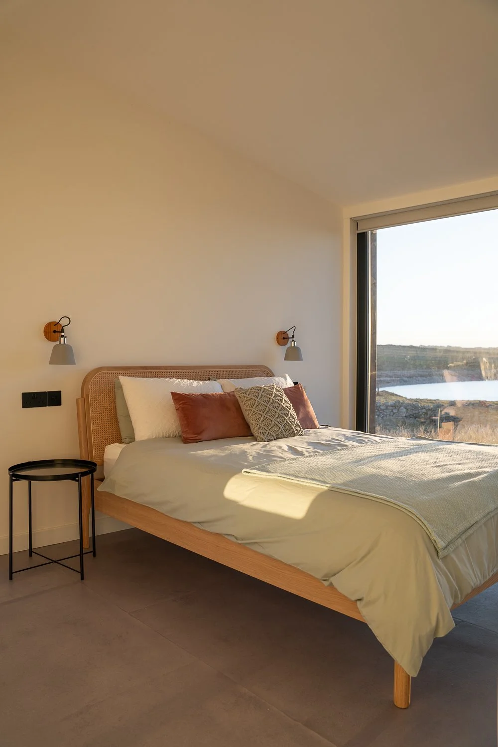 A beautifully lit bedroom during golden hour, with sunlight streaming through the floor-to-ceiling window. The warm, golden light creates a serene atmosphere, highlighting the inviting space and inviting a sense of tranquility and comfort. 