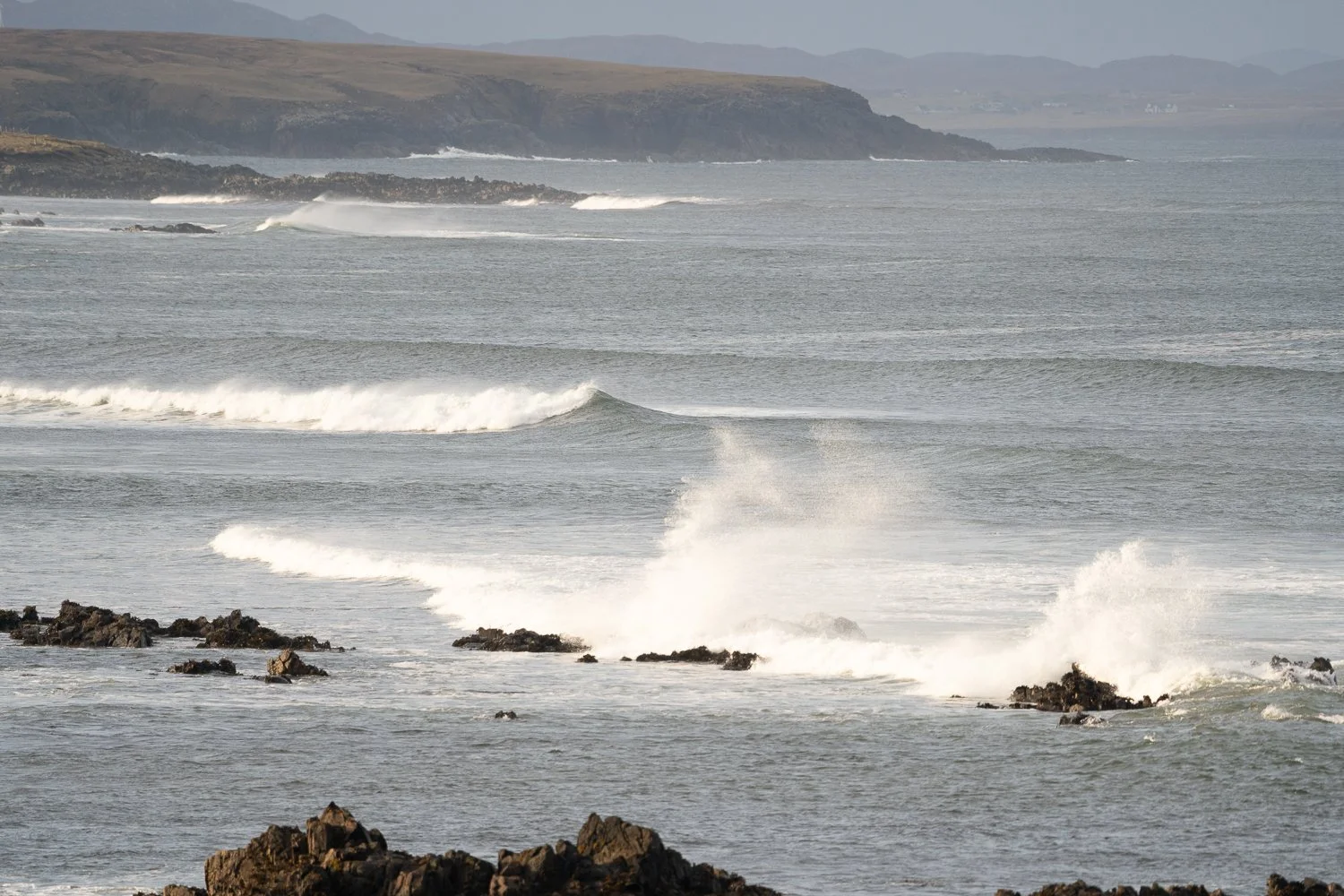 Ocean waves crashing against the rocks, with the wind creating a dynamic spray of water. This captivating scene captures the raw beauty and energy of the sea, showcasing the vibrant interplay between the waves and the elements.