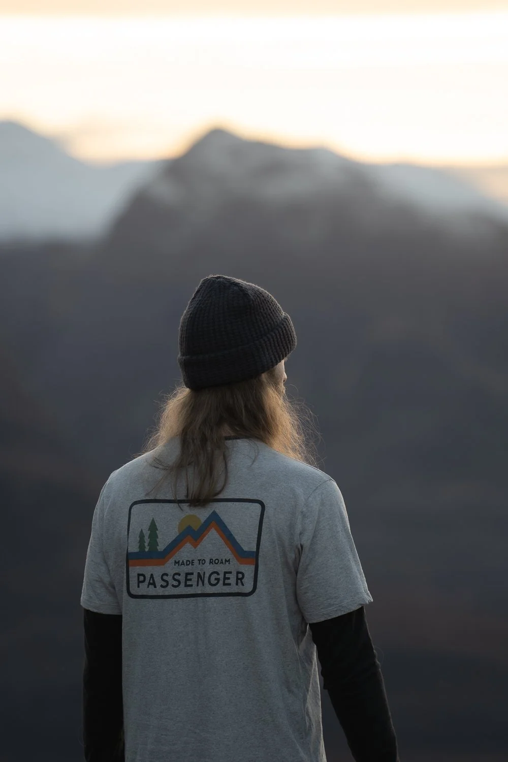 A model wearing grey cotton Passenger Clothing t-shirt while admiring the views on the top of the mountain.