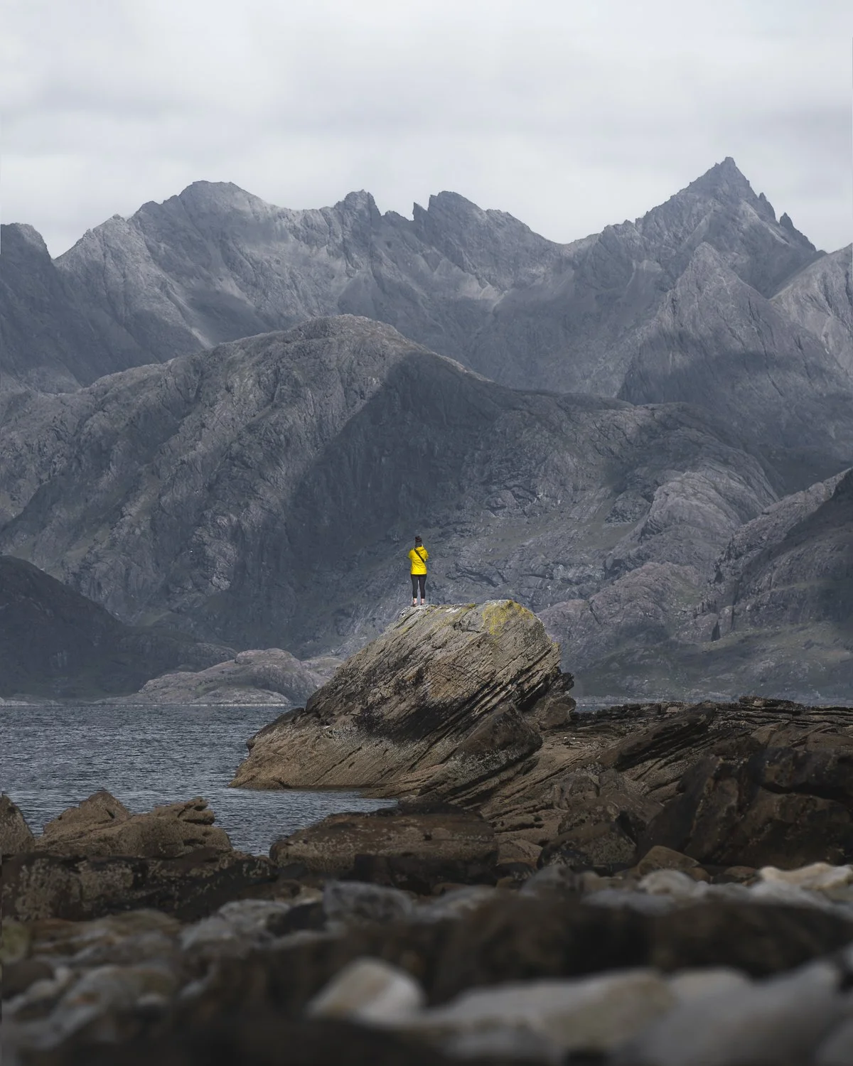 A person standing on the rock admiring jagged peaks of Cullin Range in the distance.