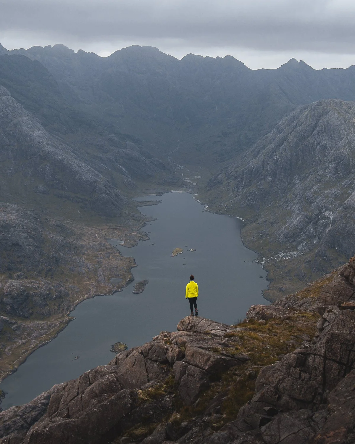 A breathtaking view of the Cuillin mountain range with Loch Coruisk below, with a person standing in the foreground, taking in the scenery.
