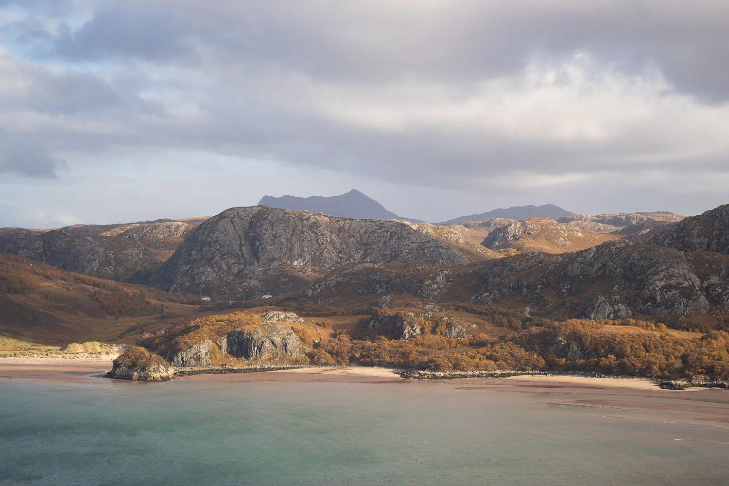 Rugged coastline with white sandy beaches and mountains behind.