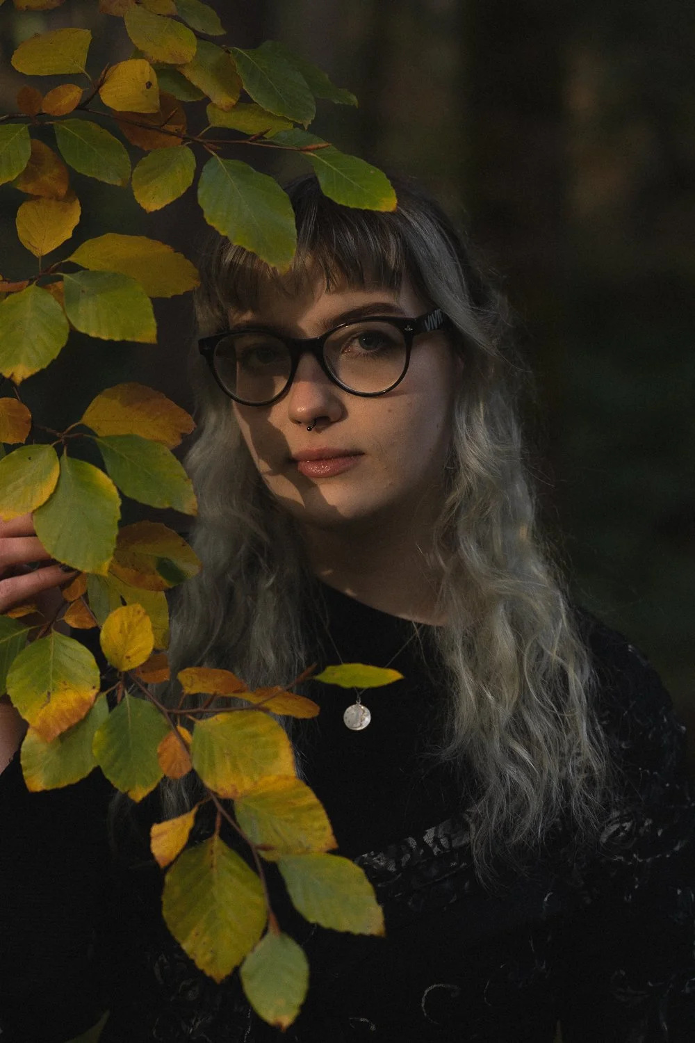 Portrait of a blonde model in glasses with leaves next to her face.