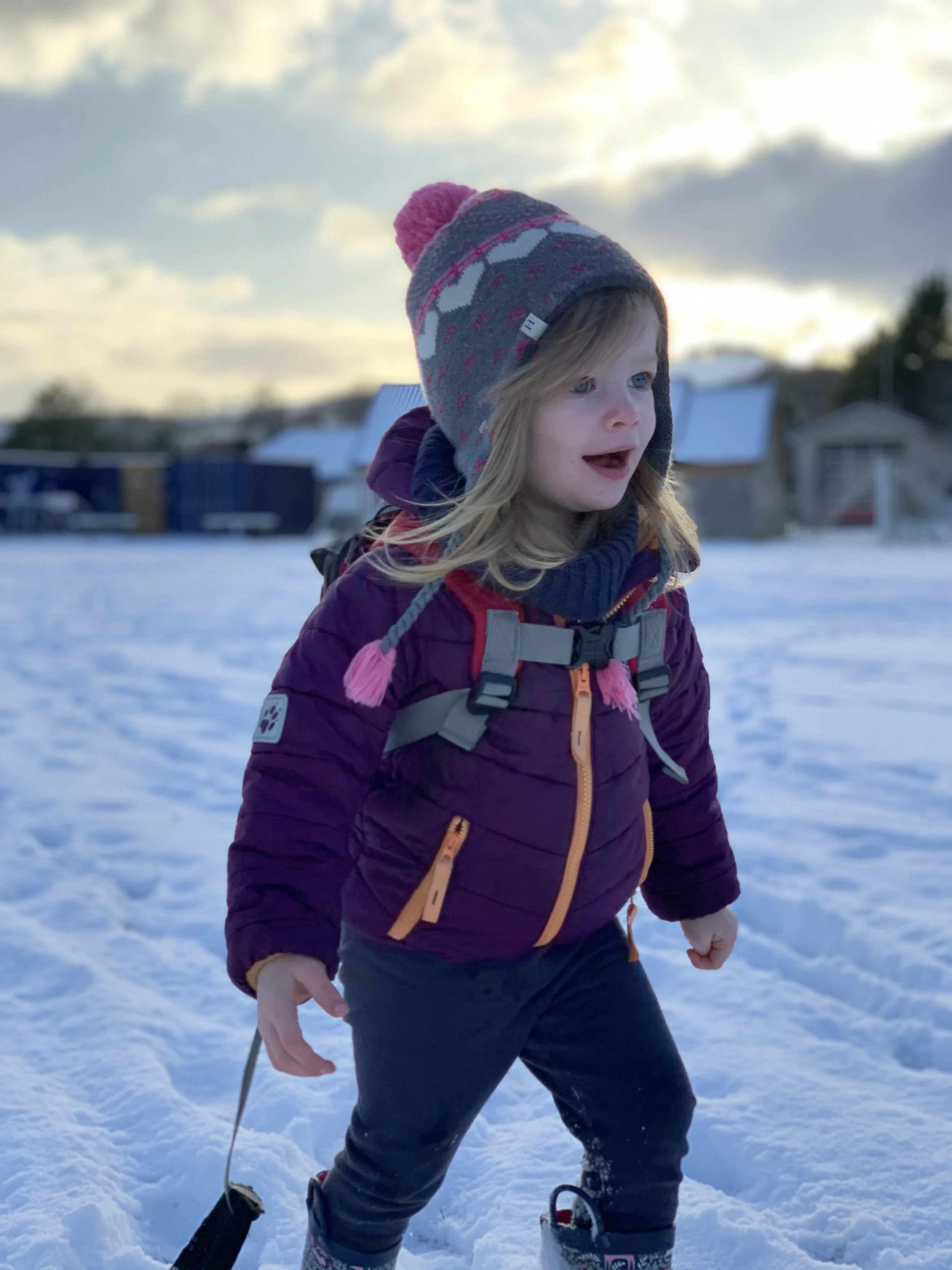 Young girl dressed in winter clothes playing in the snow outdoors during sunset