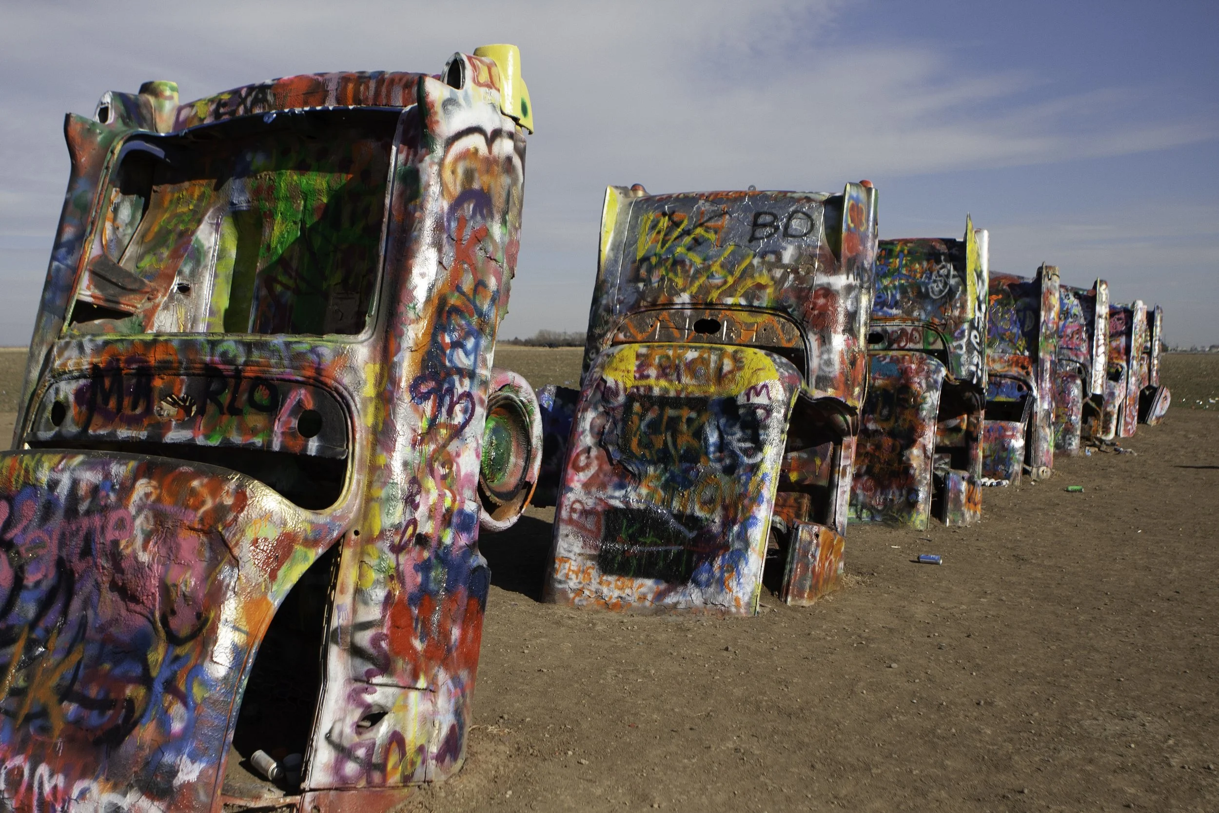 A line of old bus body shells painted with graffiti, standing in an open field.