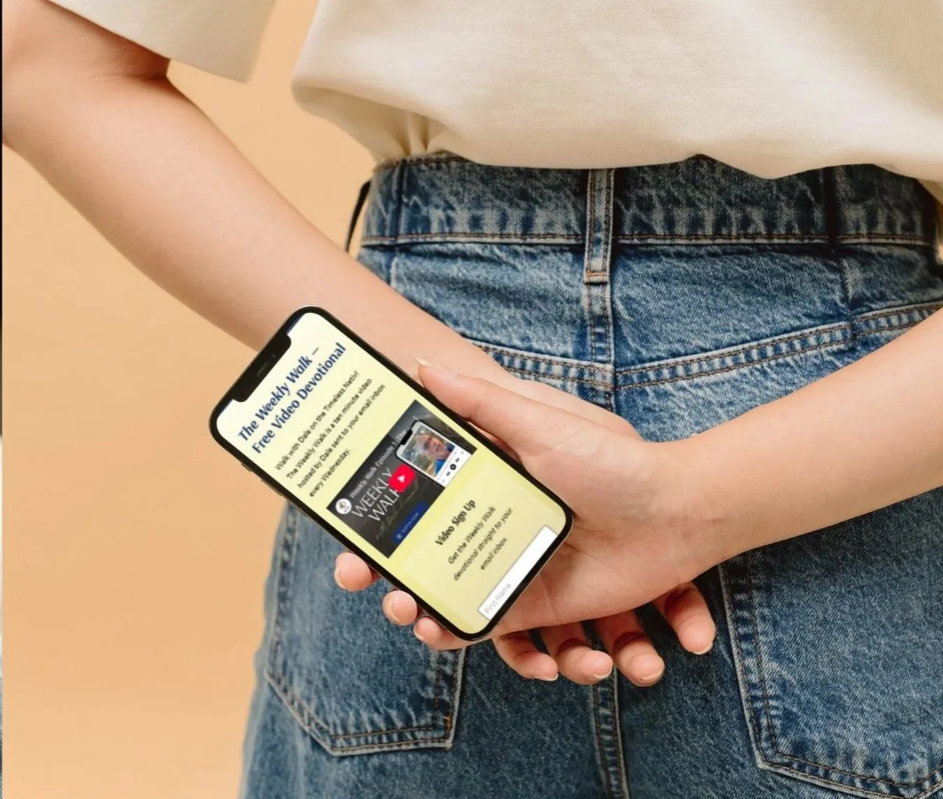 Person holding a smartphone displaying a video subscription sign-up page with text about weekly walk devotionals.