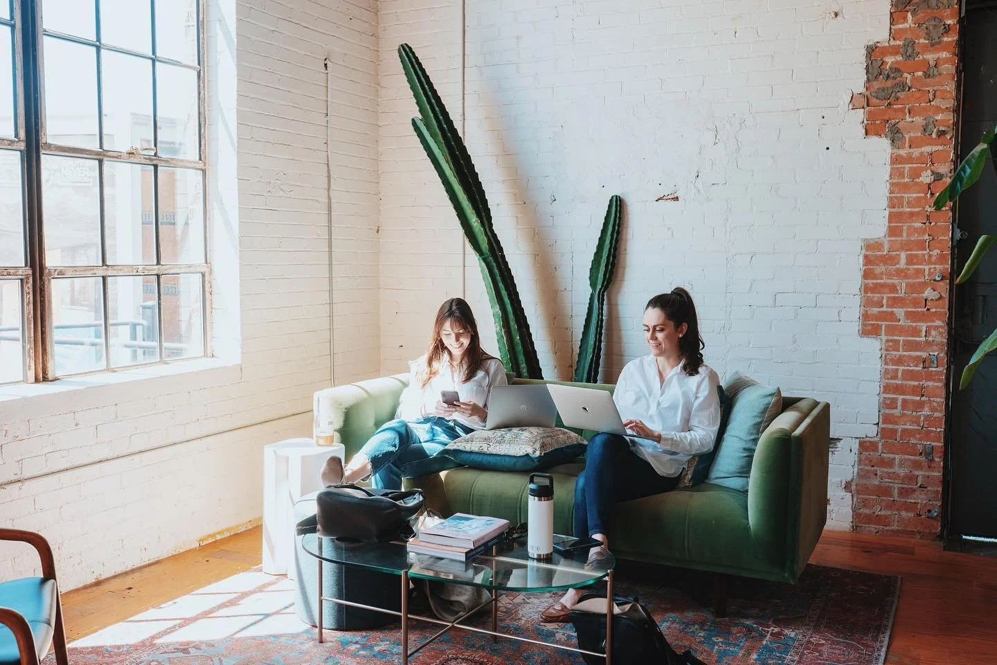 Two Wax Space members working on laptops in a sunlit brick room