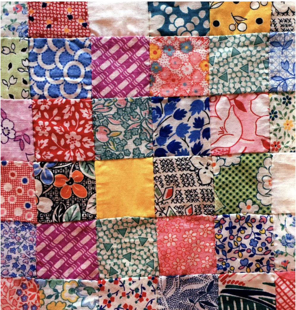 Close-up of a colorful patchwork quilt made of small square fabric pieces with various floral and geometric patterns.