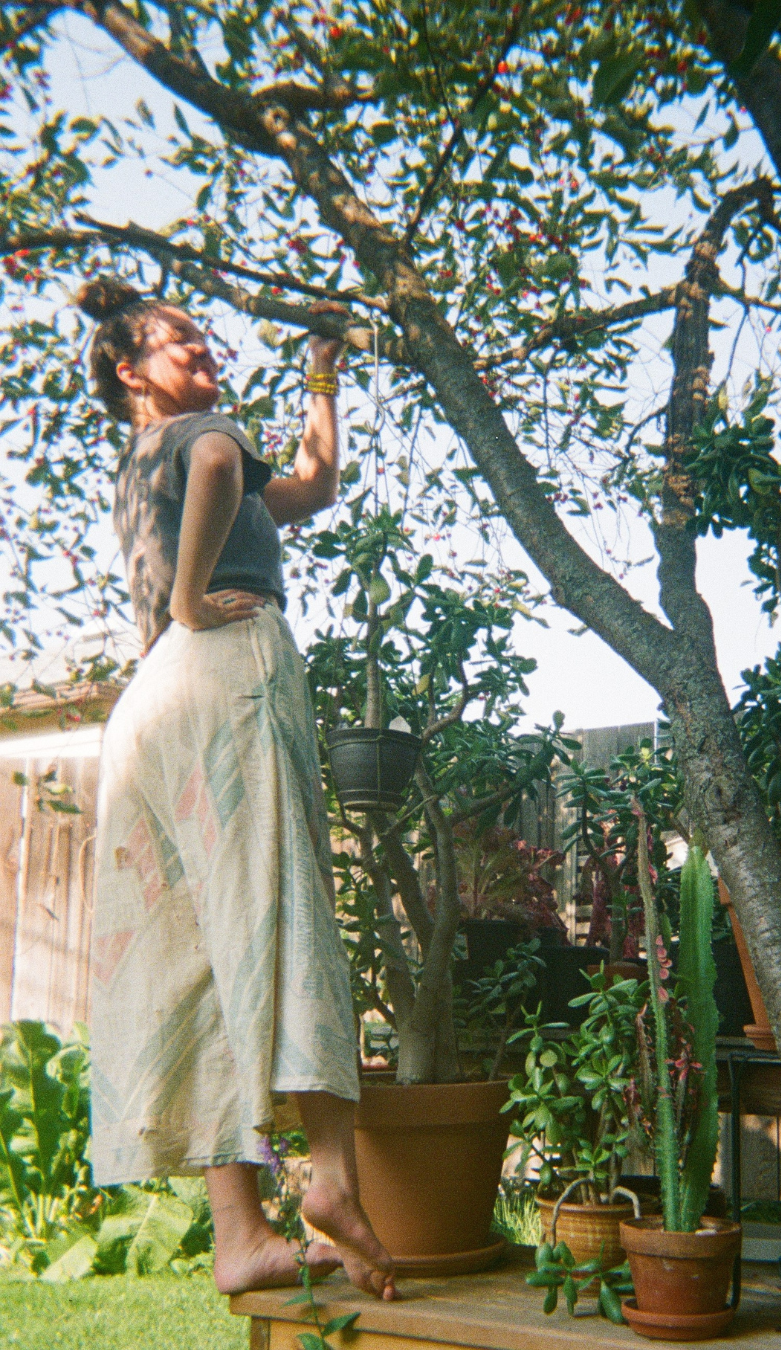 Woman pruning a tree in a backyard garden with potted plants and a wooden fence.