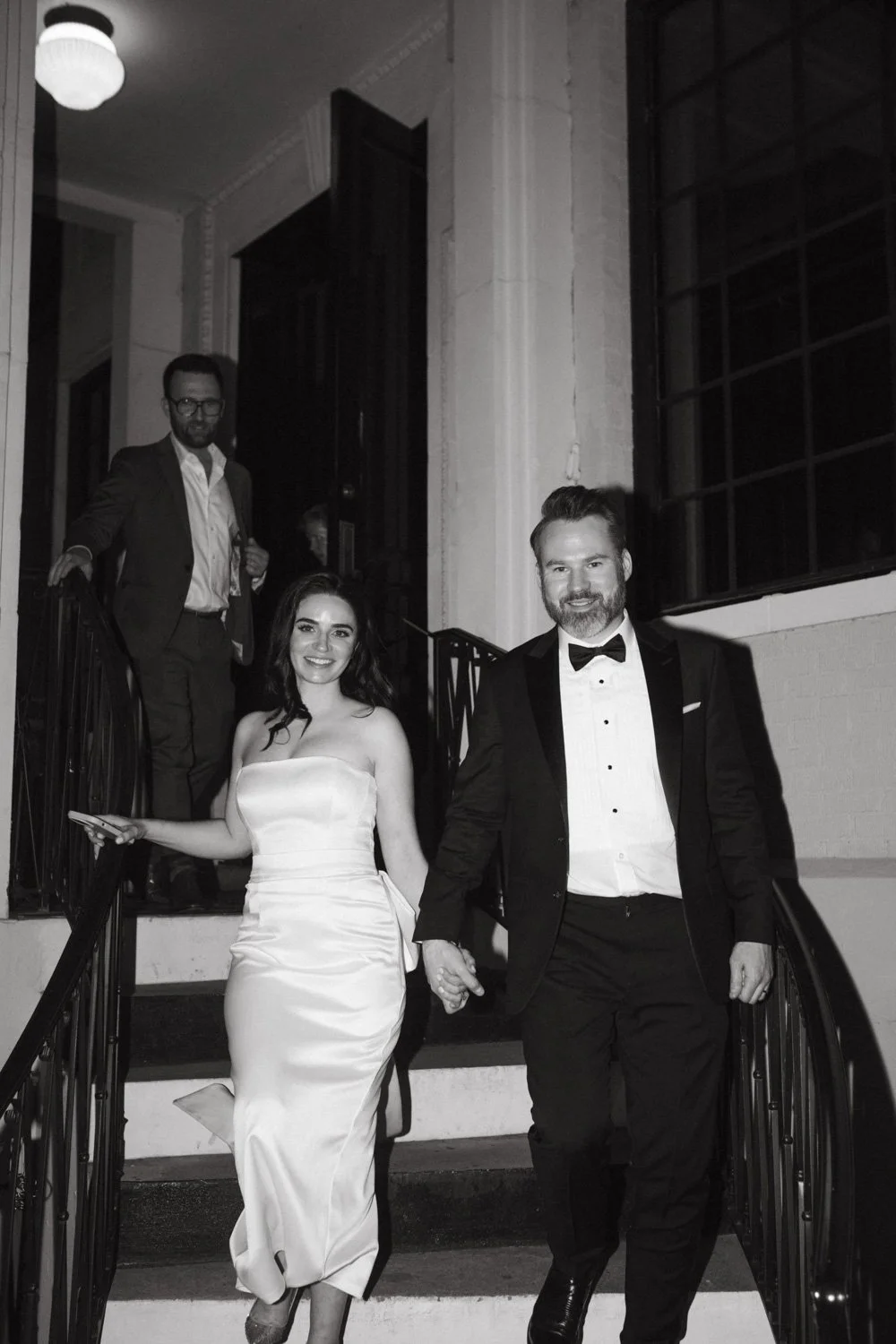 A bride in a strapless gown and a groom in a tuxedo walk down stone stairs while holding hands, captured by a Dallas wedding photographer.