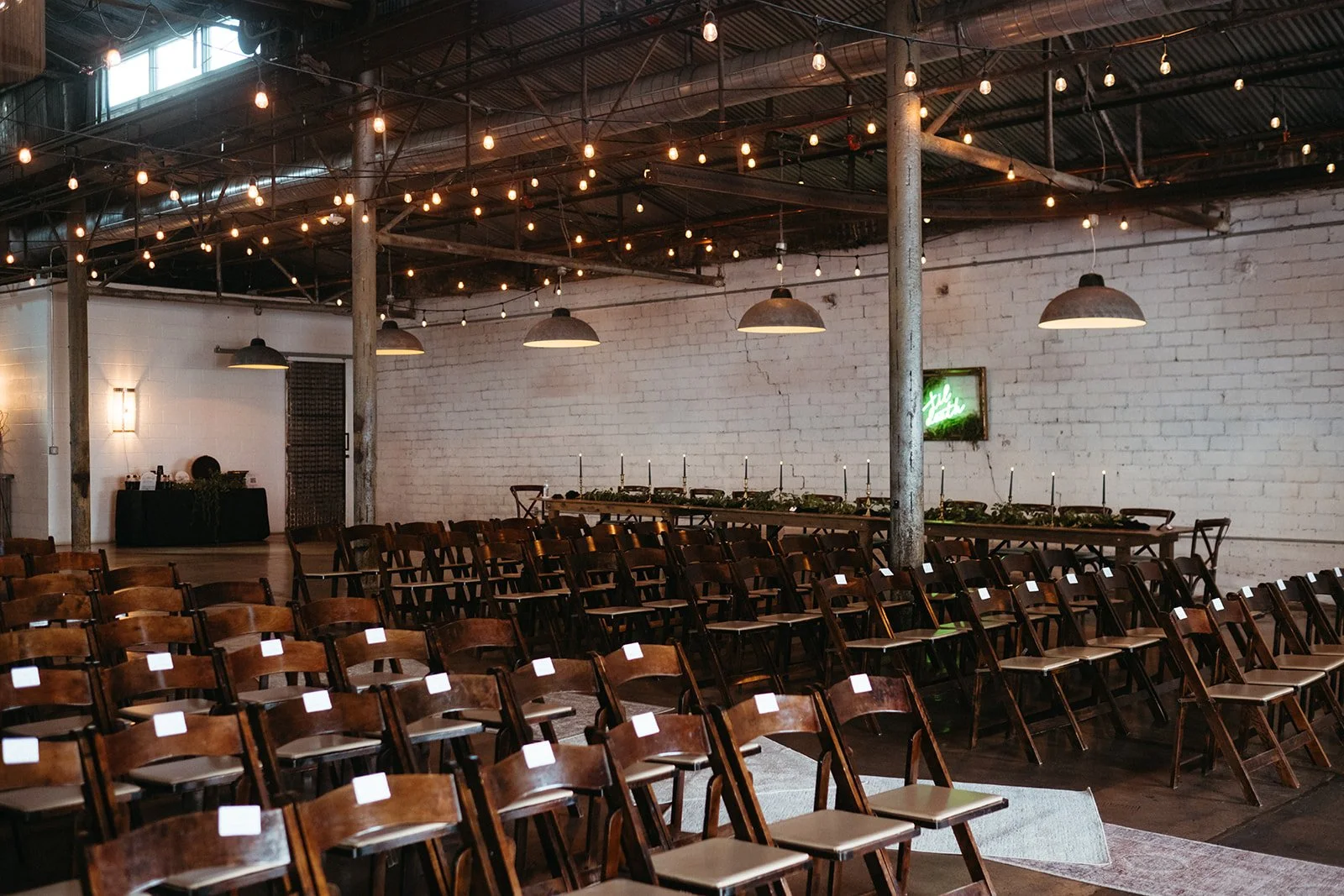 Rows of wooden folding chairs set up for a ceremony in the 4Eleven rustic event space with string lights and white brick walls.