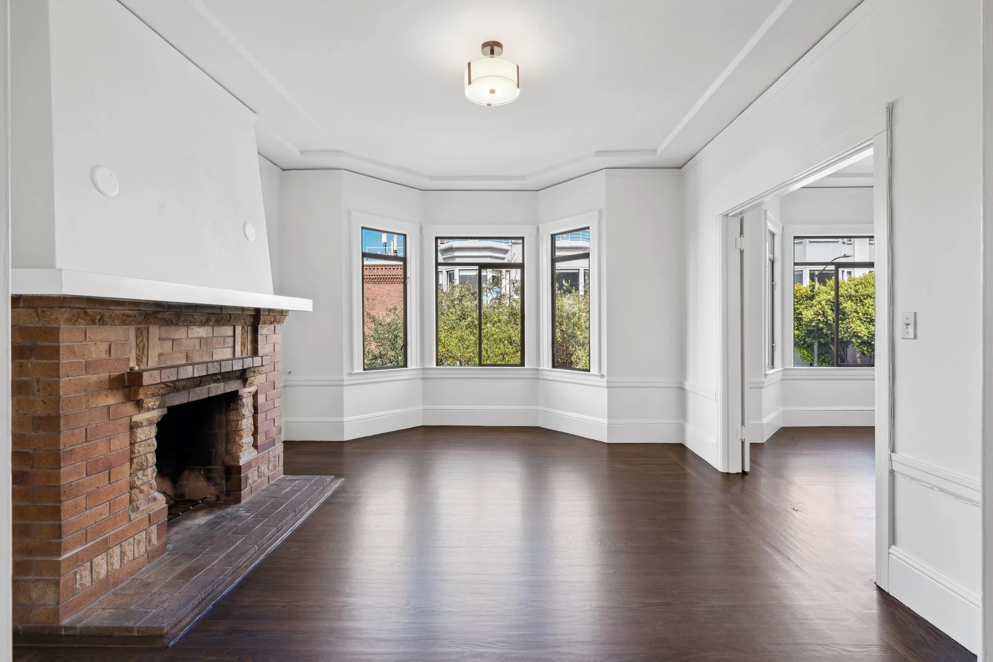 Bright living room with white walls, large windows, and a brick fireplace.