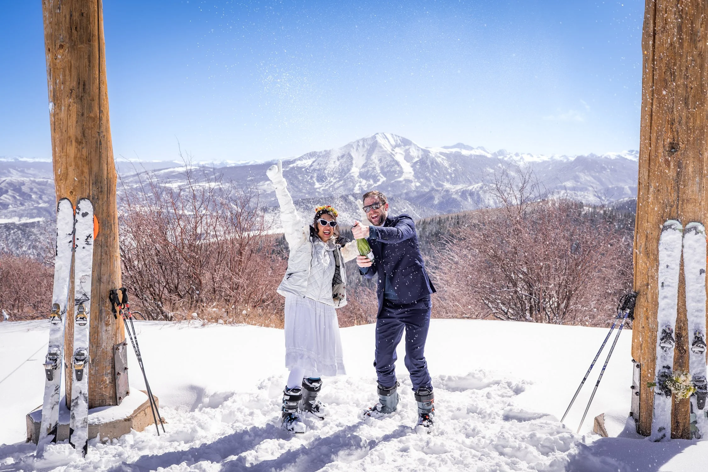 A bride and groom spray a bottle of champagne in celebration of their ski elopement day!