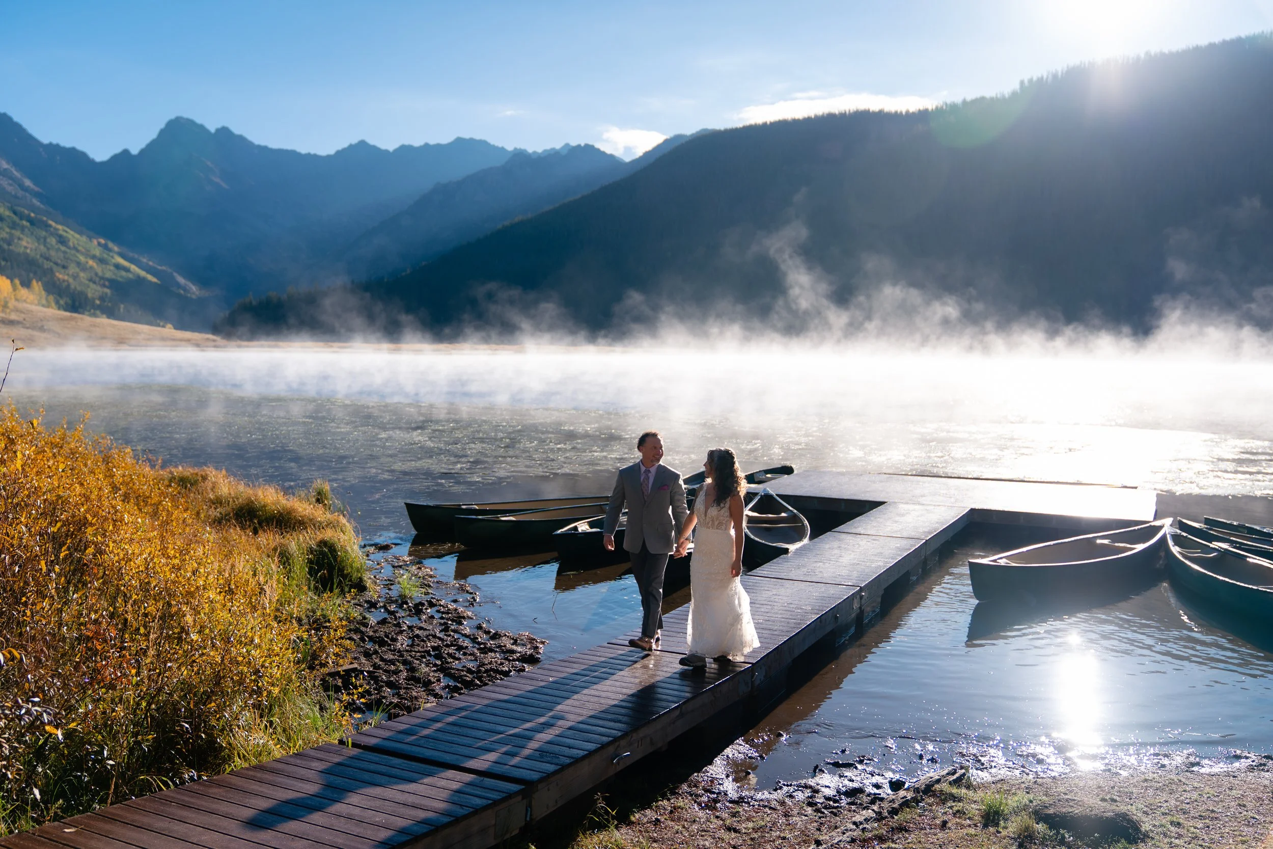 A bride and groom walk down a dock on a foggy lake in Vail, Colorado.