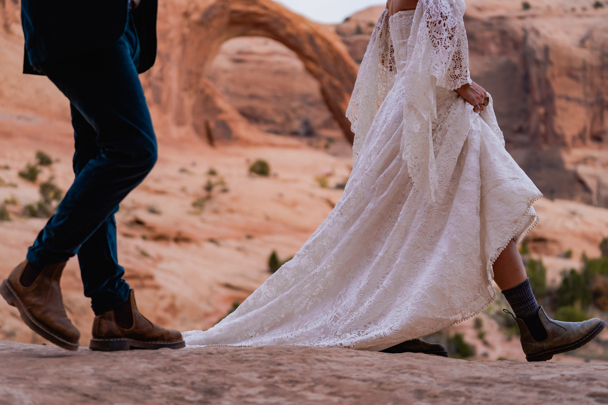 A close-up shot of the hiking shoes of a bride and groom as they walk in front of an arch in Moab, Utah.