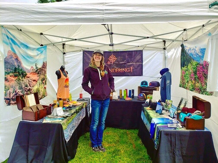 Girl smiling and standing inside a tent at a festival. Showcased are different products with landscape photography.