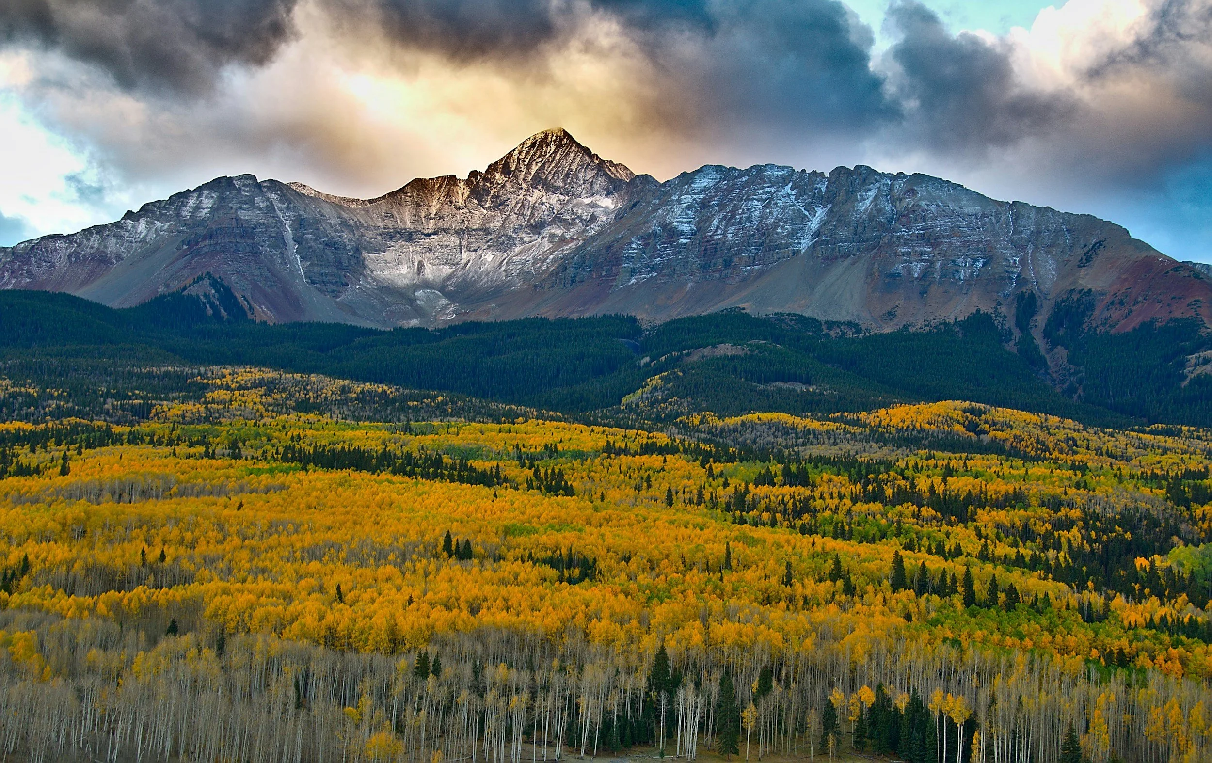 A sunset over snowy mountains and a fall-colored field.