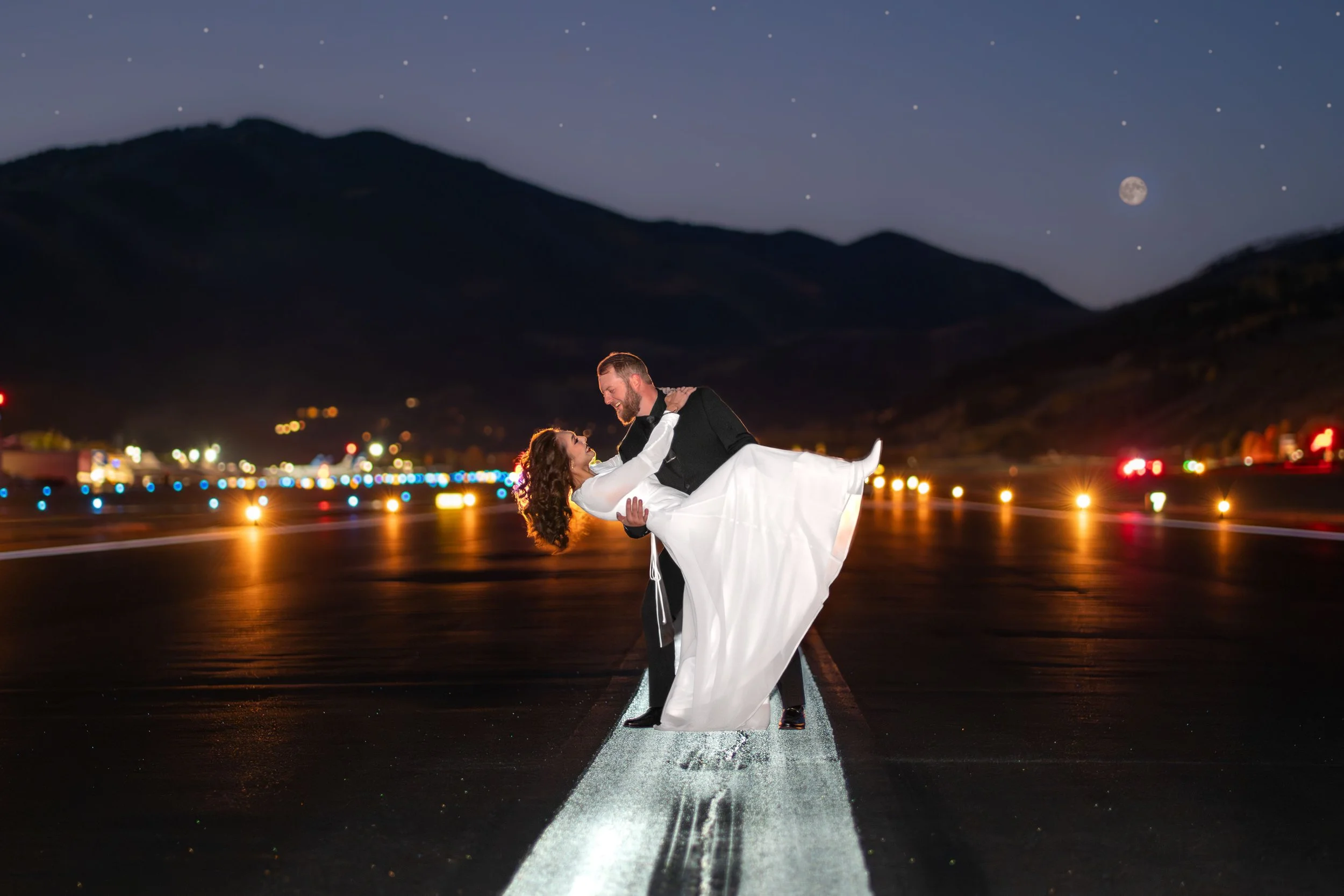 A groom holds his bride in a dipped pose on an airport runway in Aspen, Colorado.