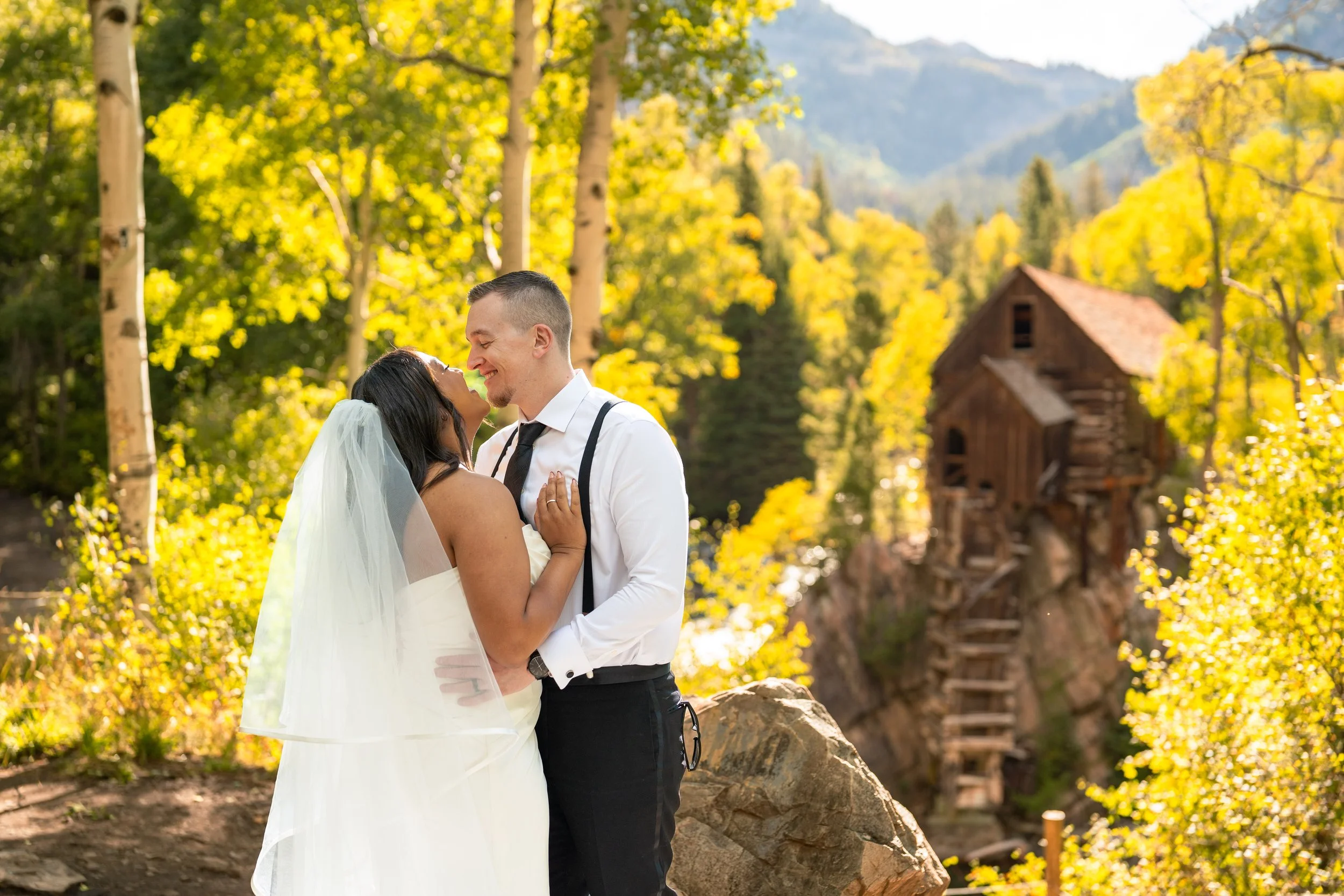 A wedding couple holds each other, smiling, in golden aspen trees in Marble, Colorado. Crystal Mill is behind them.