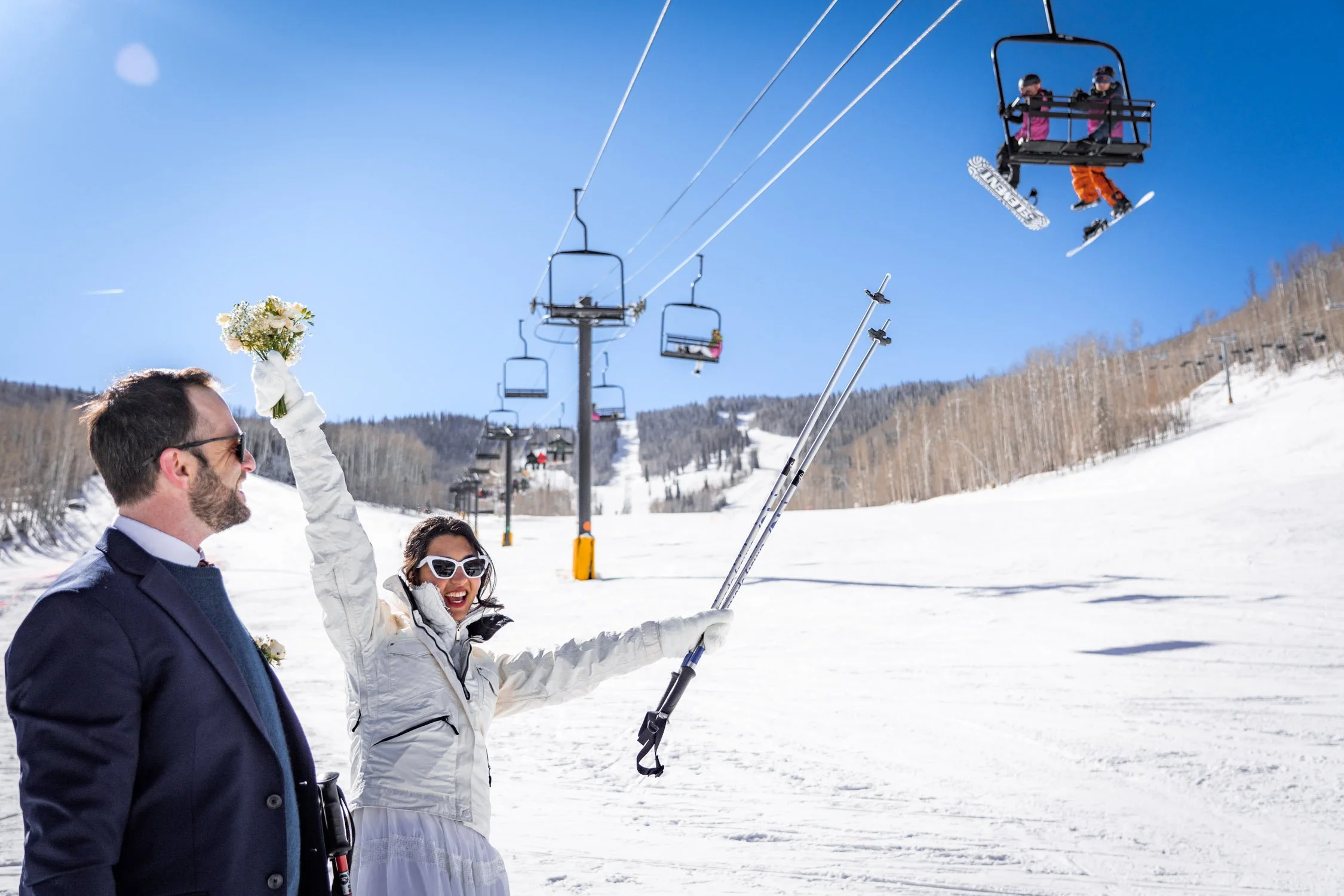 A bride and groom cheers under a ski lift on their wedding day.