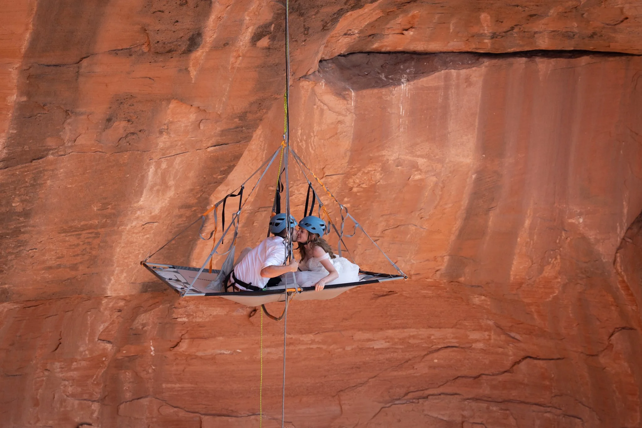 A bride and groom kiss on a rock climbing suspended portaledge in Moab, Utah.