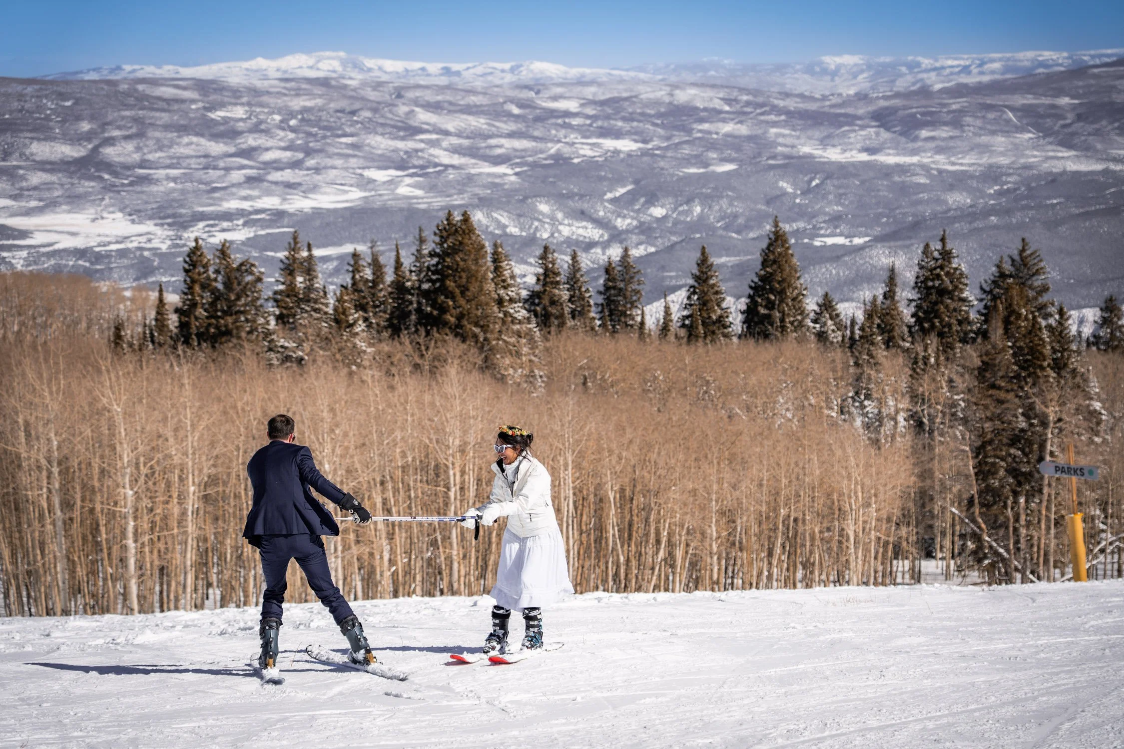 A bride and groom have fun down a ski slope in Colorado.