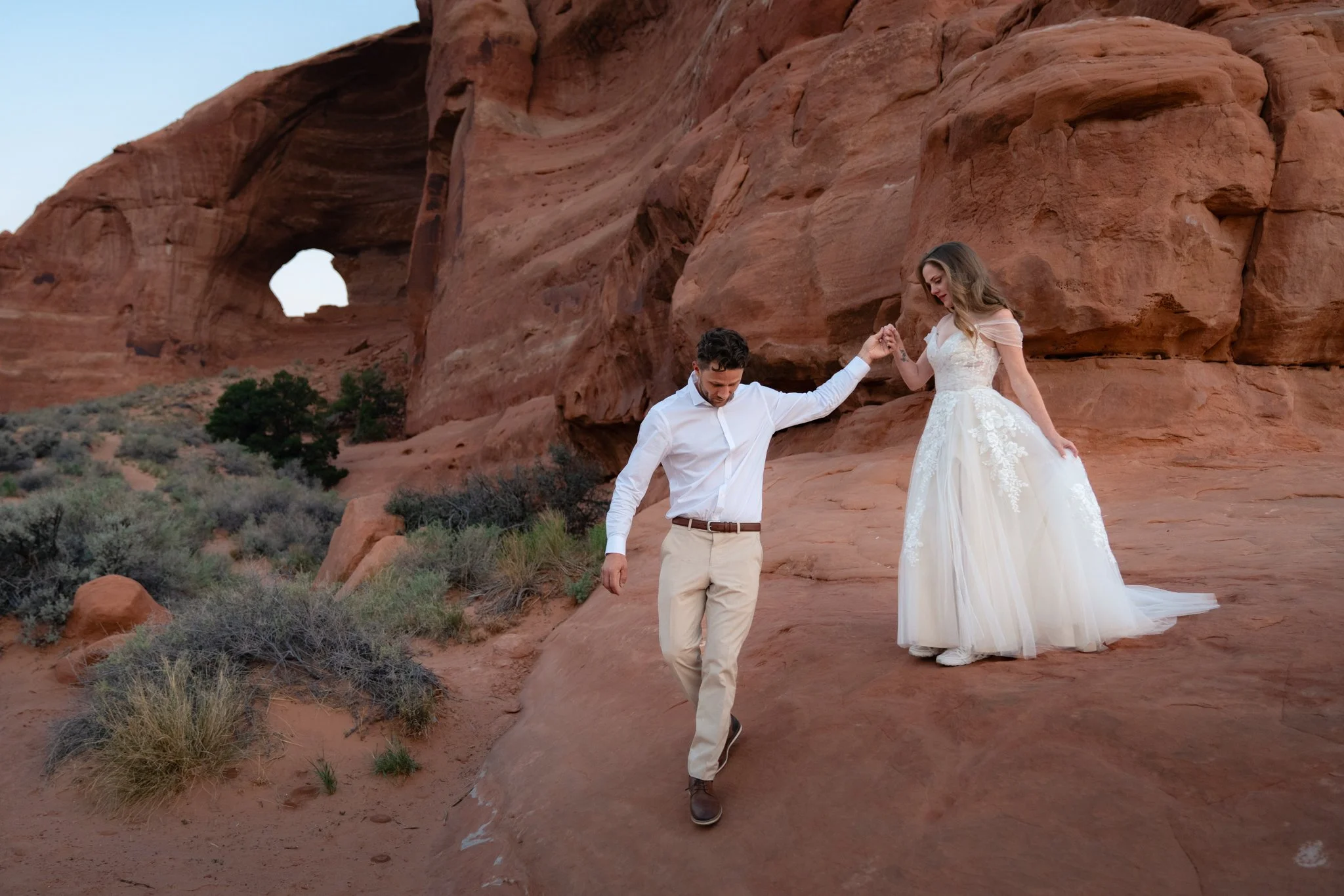 A groom leads a bride down red rock in Moab.